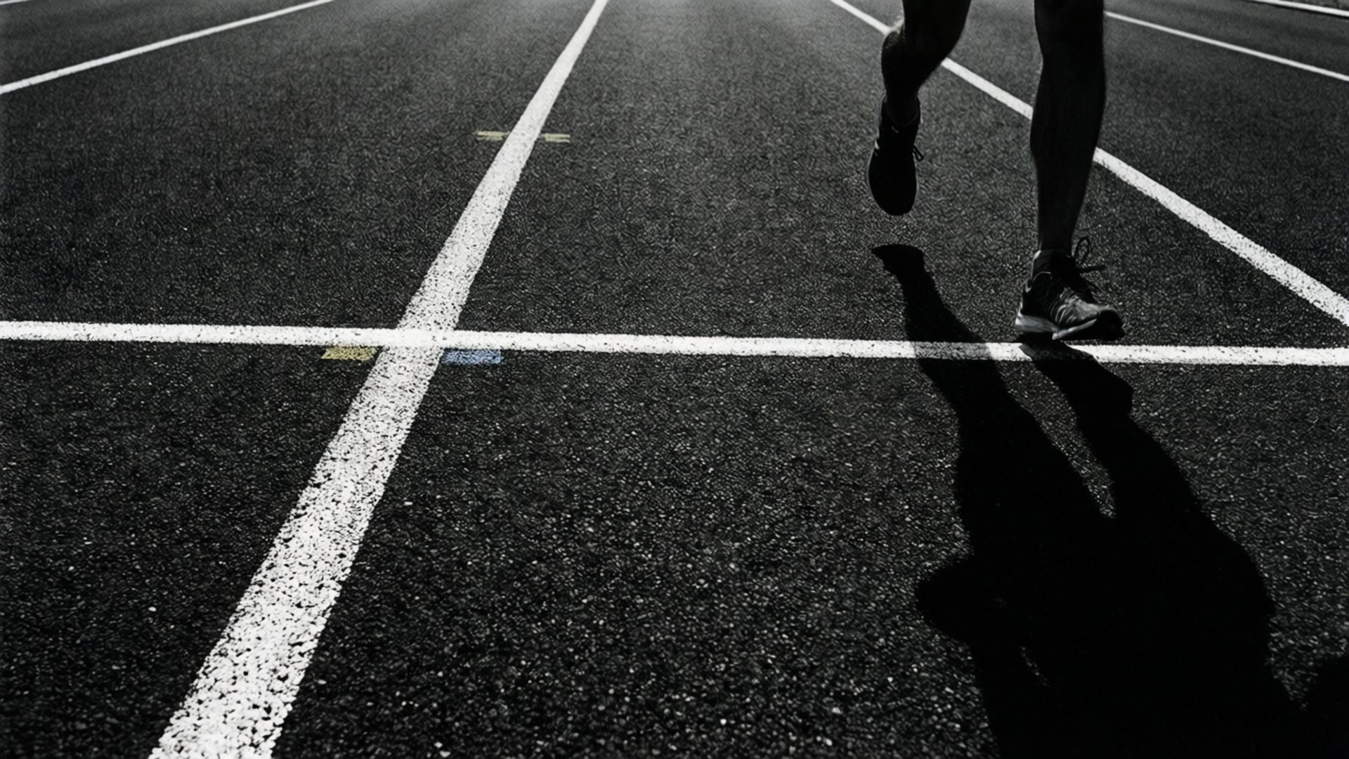 Finish Line 桌布 壁紙 — 低角度黑白拍攝，跑者雙腿越過跑道終點線，拖出長長影子。