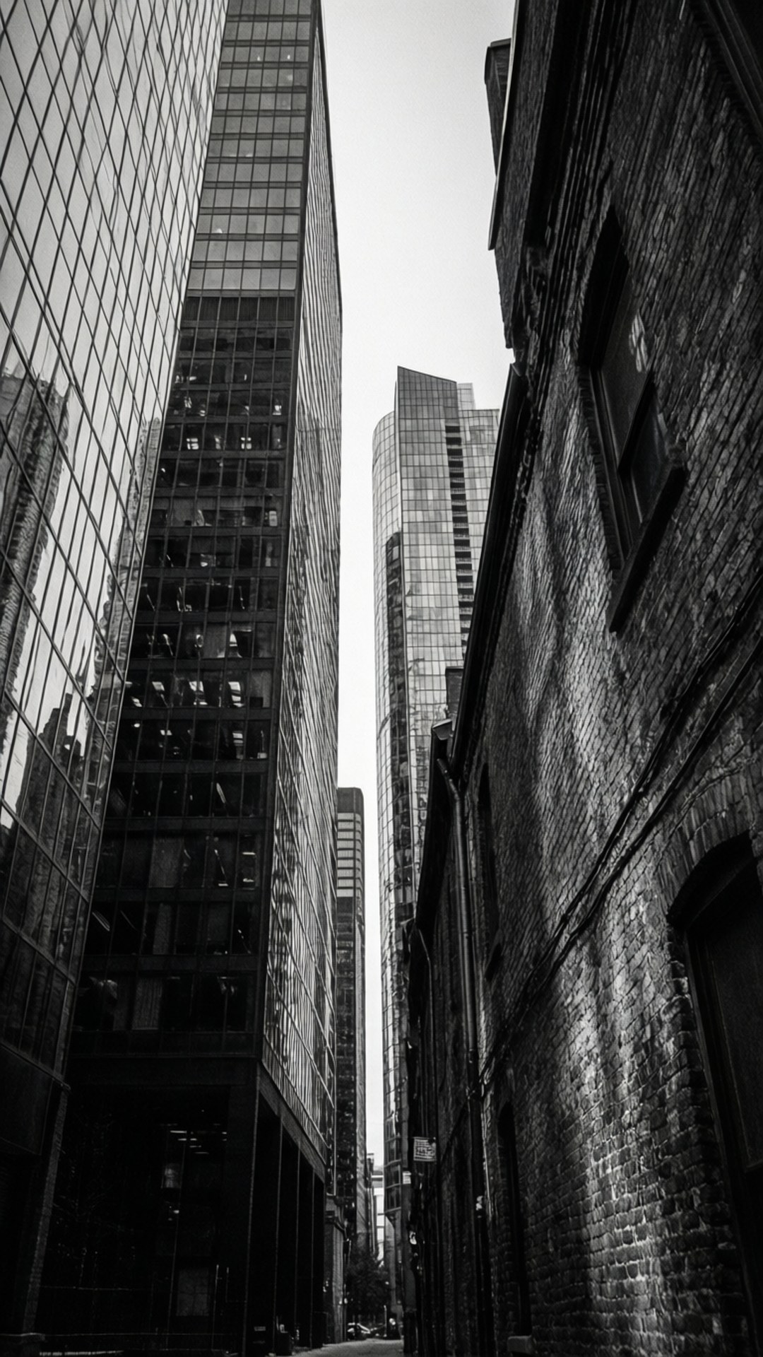 Downtown Contrast in Black and White 壁紙 — 低角度黑白照片捕捉到高聳的玻璃摩天大樓，夾著一條狹窄的小巷，旁邊是一座風化的磚砌建築。