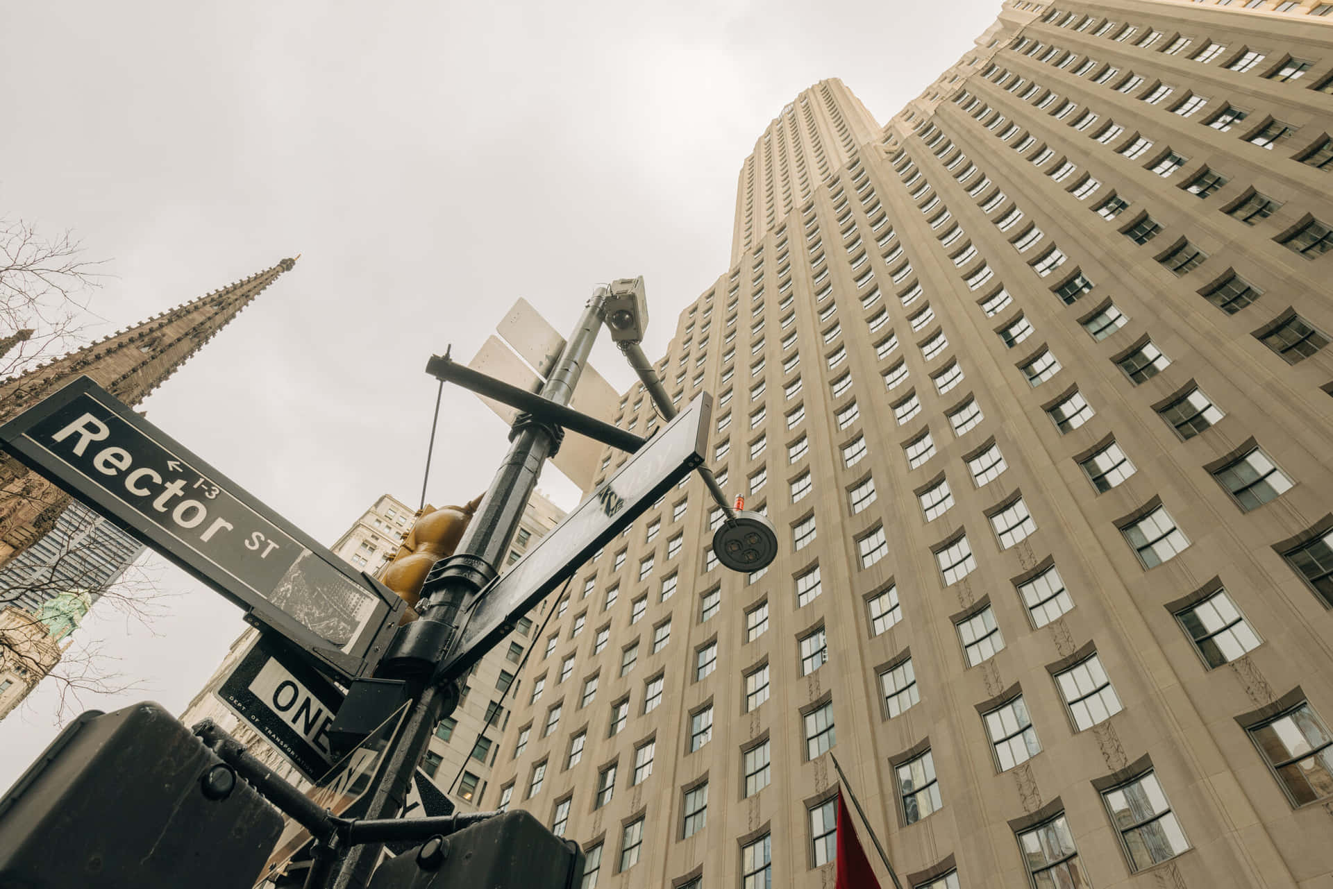  壁紙 — 低角度拍攝Rector Street路牌，背景是高聳的米色摩天大樓和哥德式尖塔，天空陰沉。