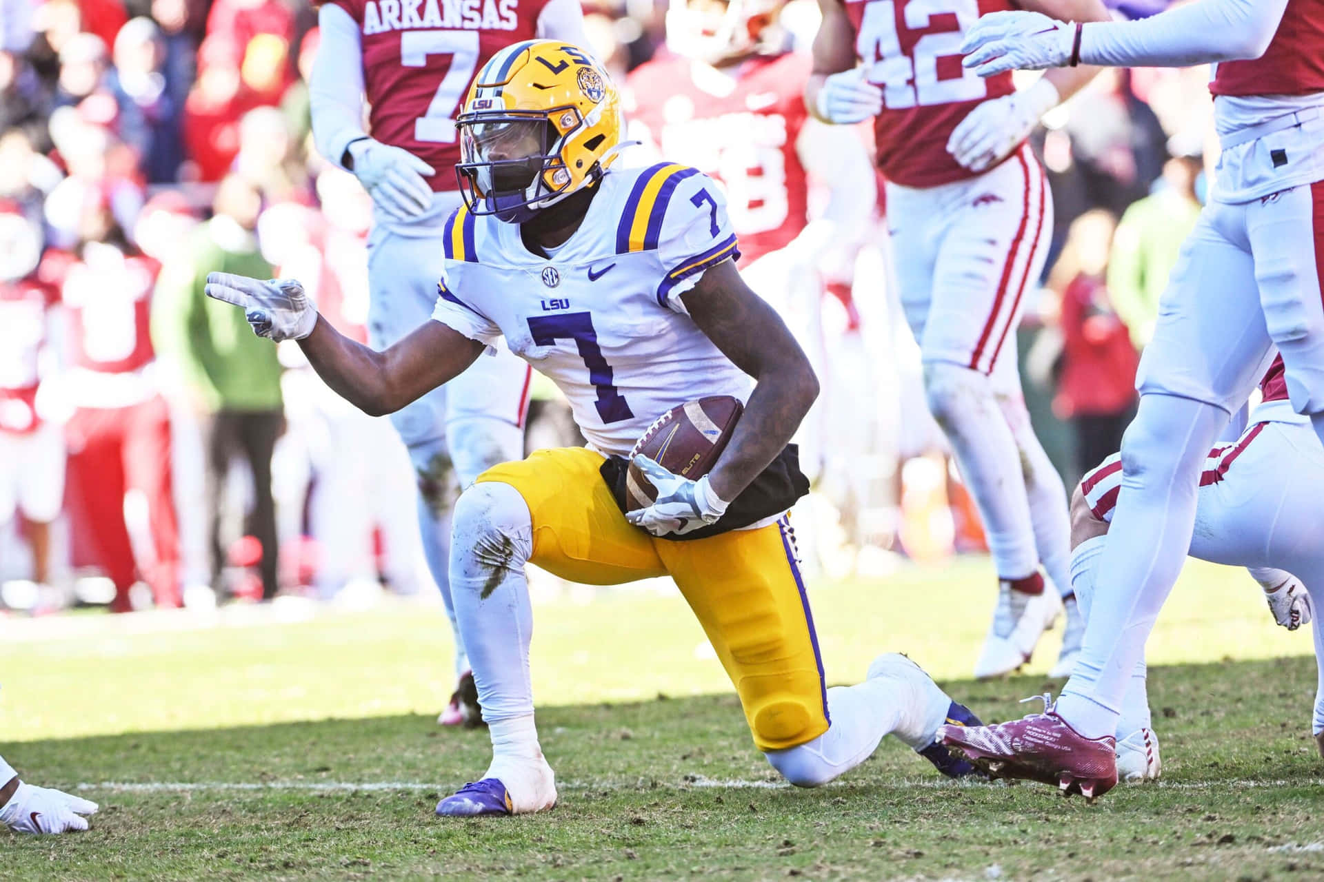  壁紙 — LSU 足球員 7 號身穿黃色和紫色裝備，在陽光明媚的球場上對陣阿肯色州的比賽中帶球衝刺。