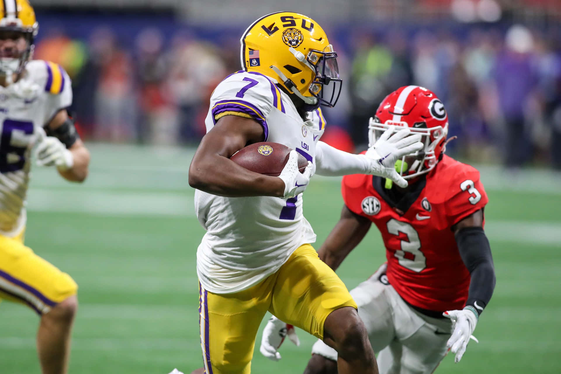  壁紙 — LSU 足球員戴著黃色頭盔、身穿白色球衣，在夜間比賽中持球奔跑，而身穿紅色球衣的喬治亞州防守球員正在逼近。