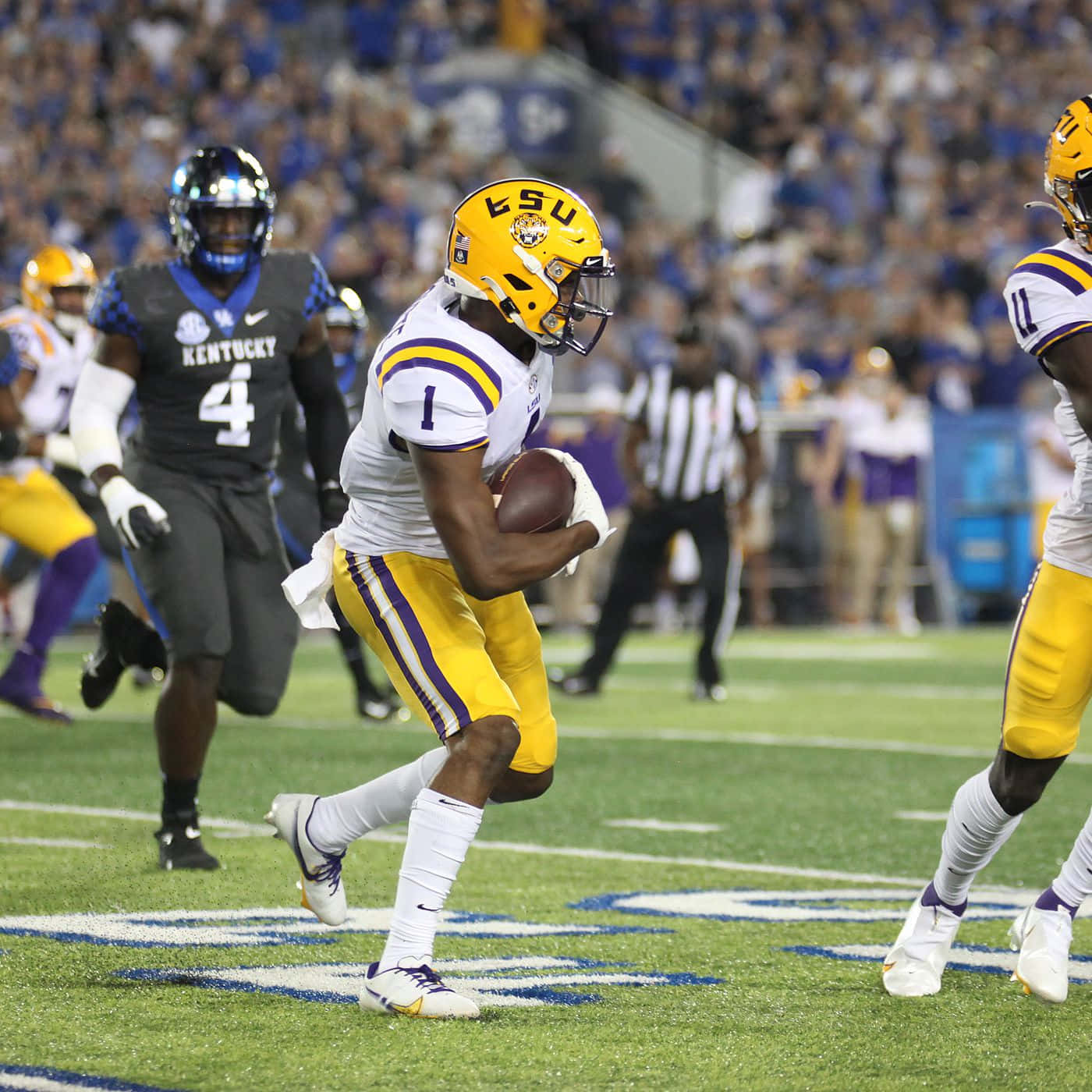  壁紙 — LSU 足球員一號帶球衝刺，肯塔基防守球員在球場燈光下逼近。