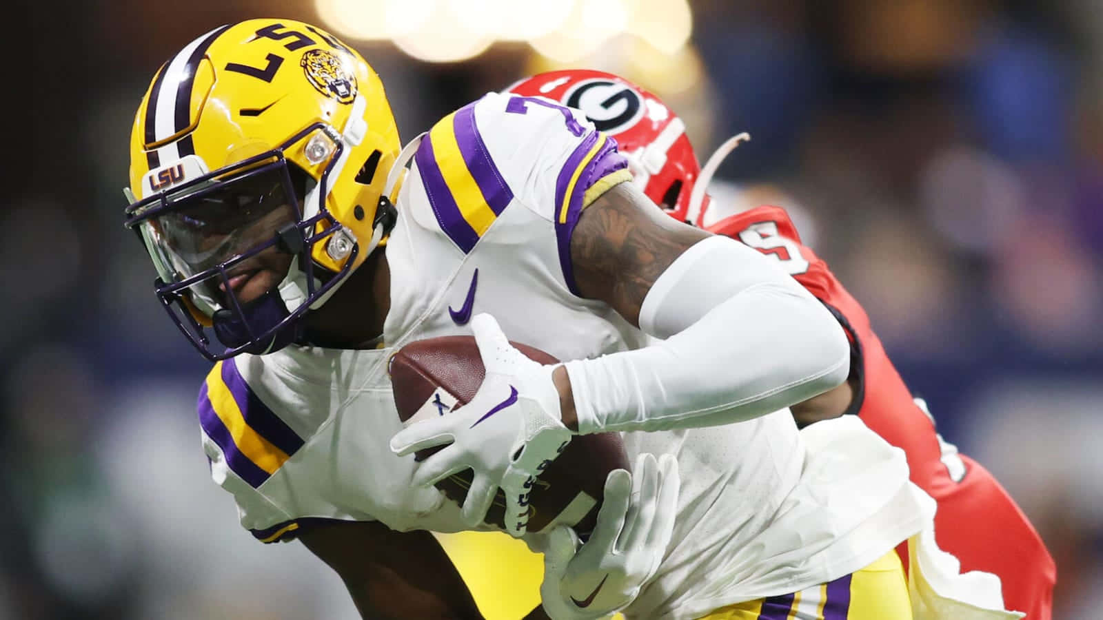  壁紙 — LSU 足球員戴著黃色頭盔，在被紅色喬治亞州防守球員攔截時緊抱住球。