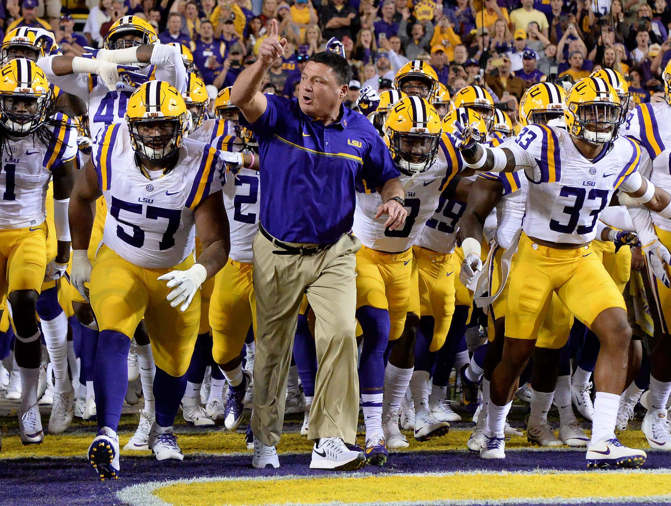 Athletic 桌布 壁紙 — LSU 美式足球教練和球員身穿紫色和金色球衣，充滿活力地衝入球場。
