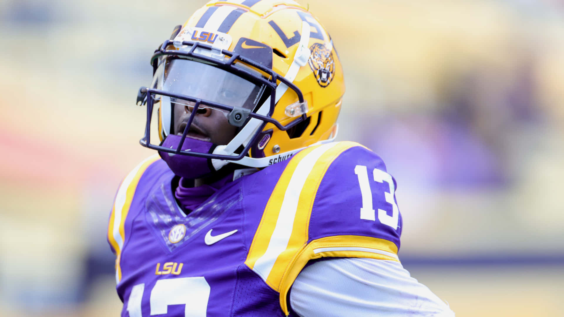 Athletic 桌布 壁紙 — LSU 足球員的特寫，身穿紫色和金色球衣，肩膀上有13號。