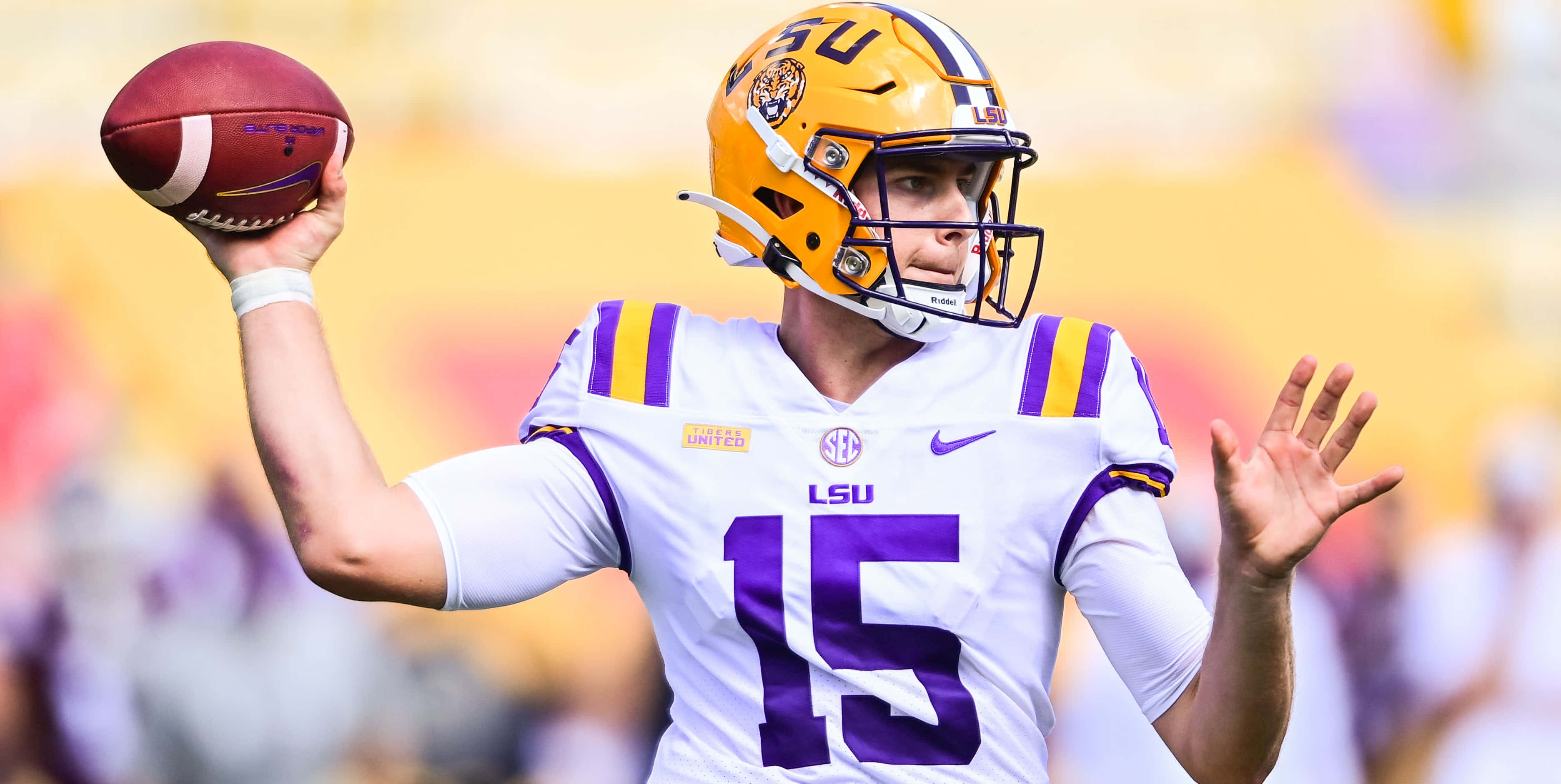 Athletic 桌布 壁紙 — LSU 足球四分衛身穿白色和紫色制服，在陽光明媚的比賽中準備投球。