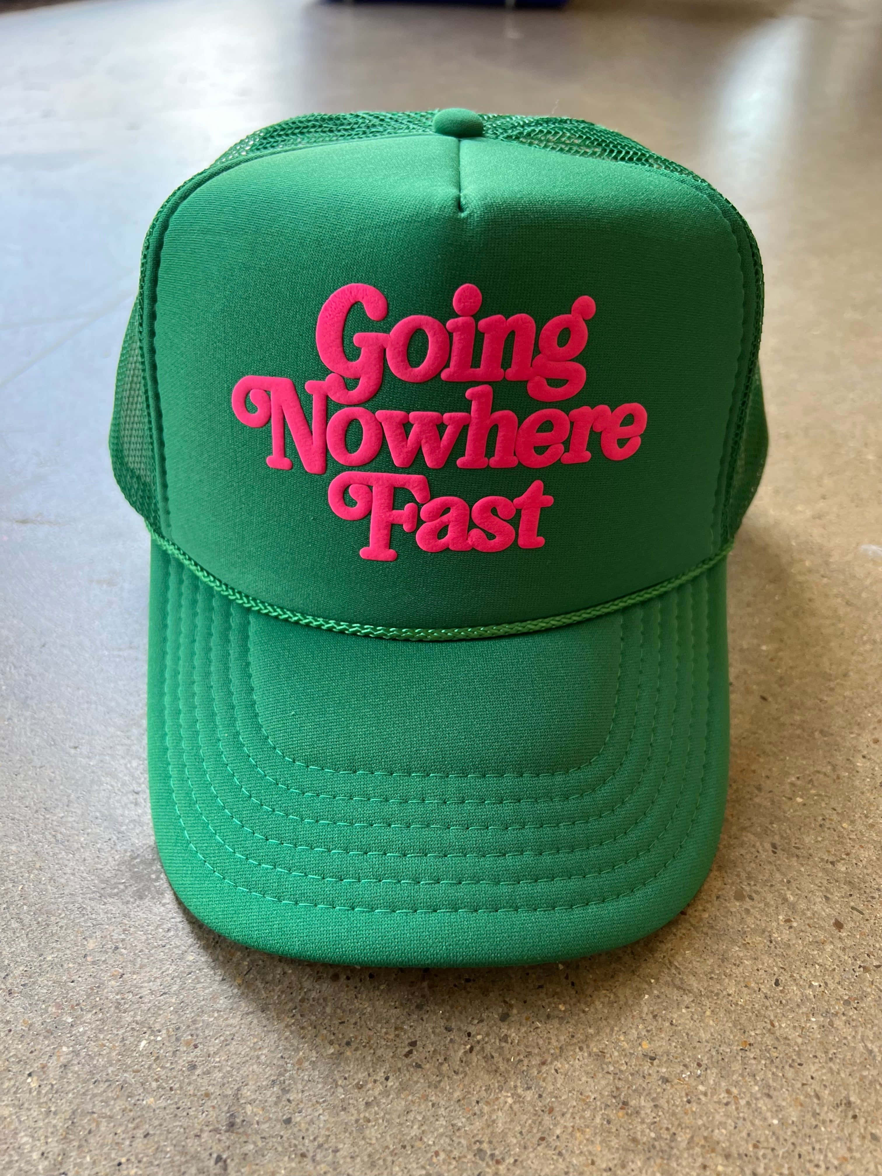 Hat 桌布 壁紙 — 一頂鮮綠色卡車司機帽，上面有鮮粉紅色刺繡文字「Going Nowhere Fast」，放在有斑點的櫃檯上。