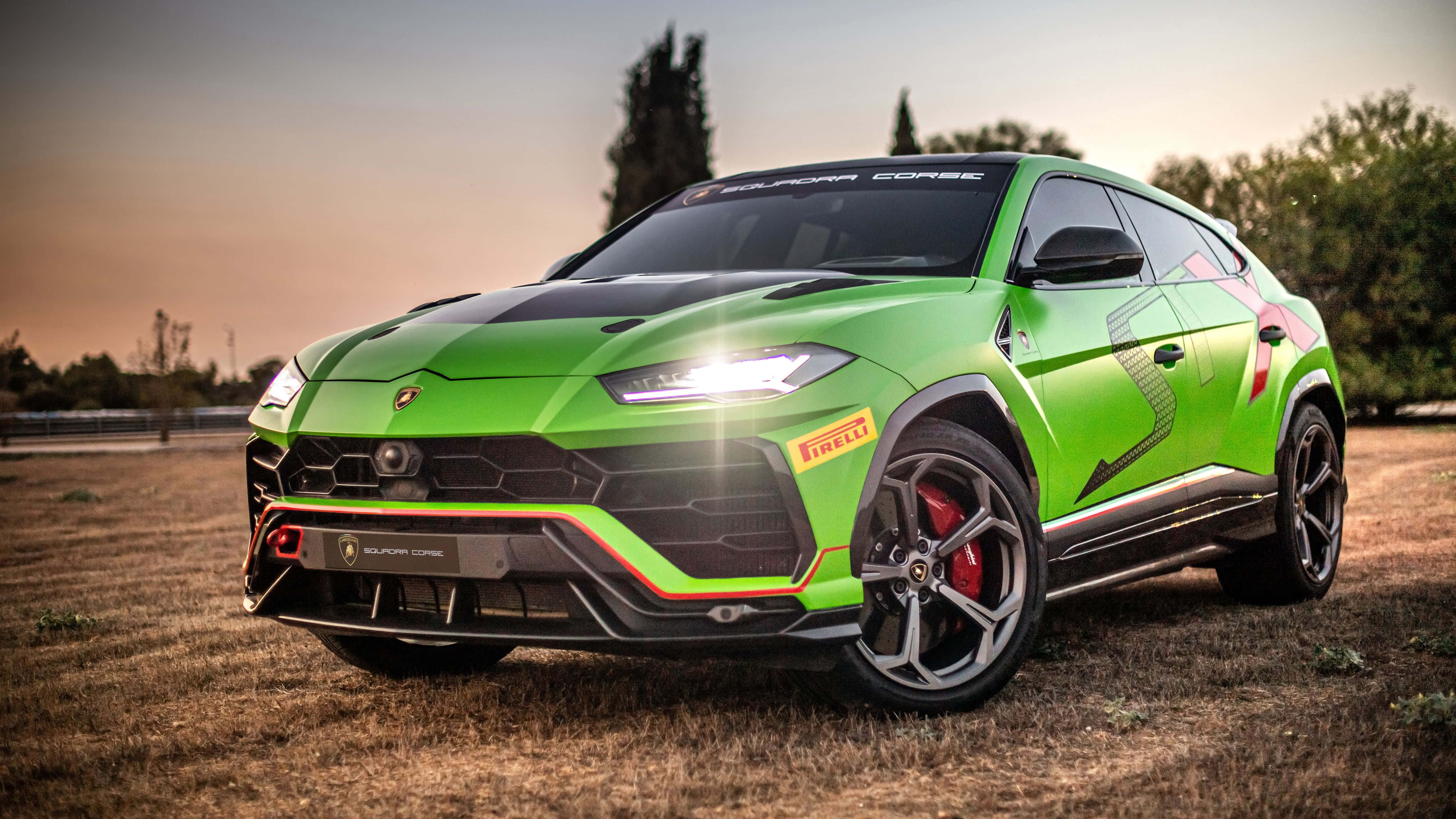 Lamborghini Urus 桌布 壁紙 — 一輛充滿活力的綠色藍寶堅尼 Urus Performante 在日落時分停在乾草地上，車頭燈閃爍，紅色制動卡鉗清晰可見。