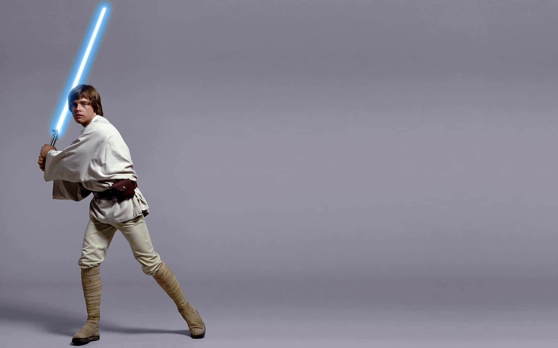 A New Hope 桌布 壁紙 — Luke Skywalker 以戰鬥姿態站立，手持發光的藍色光劍，背景是純灰色攝影棚。