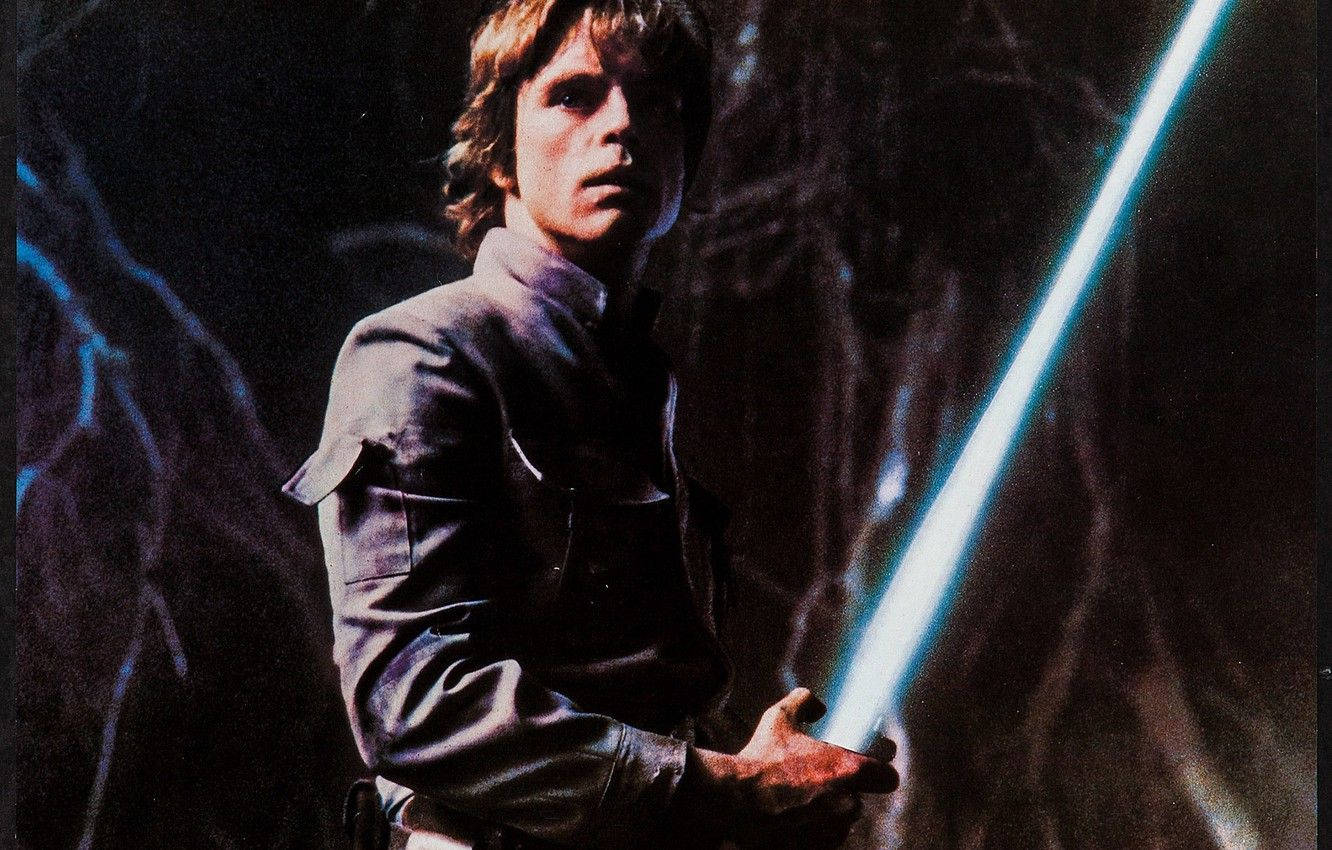 Star Wars Luke Skywalker 4K 桌布 壁紙 — Luke Skywalker 在黑暗洞穴中手持發光的藍色光劍，帶有戲劇性的燈光和強烈的表情。