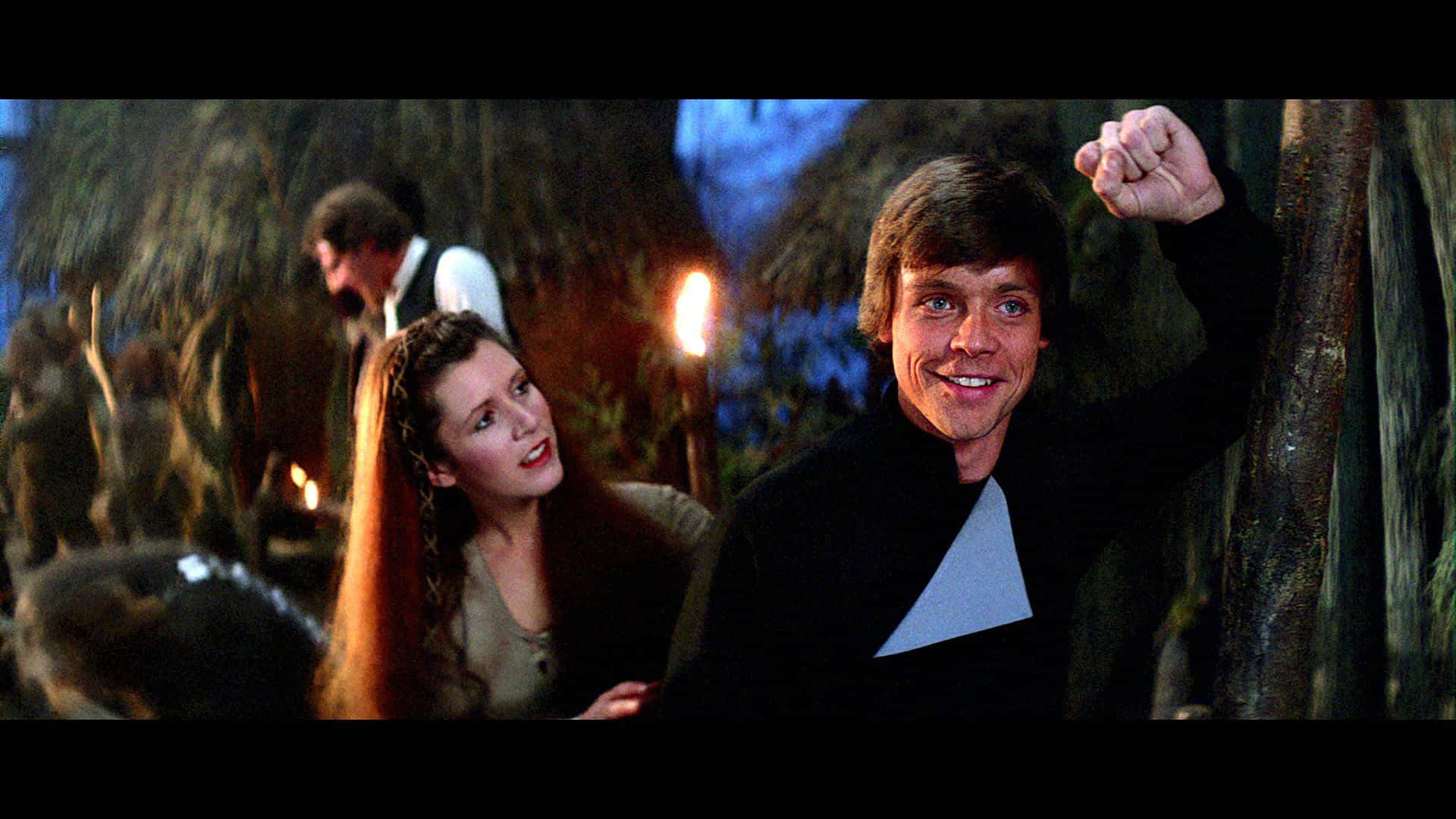 Return Of The Jedi 桌布 壁紙 — Luke Skywalker 在火炬照亮的昏暗叢林營地中，在Leia Organa旁邊舉起拳頭勝利地微笑。