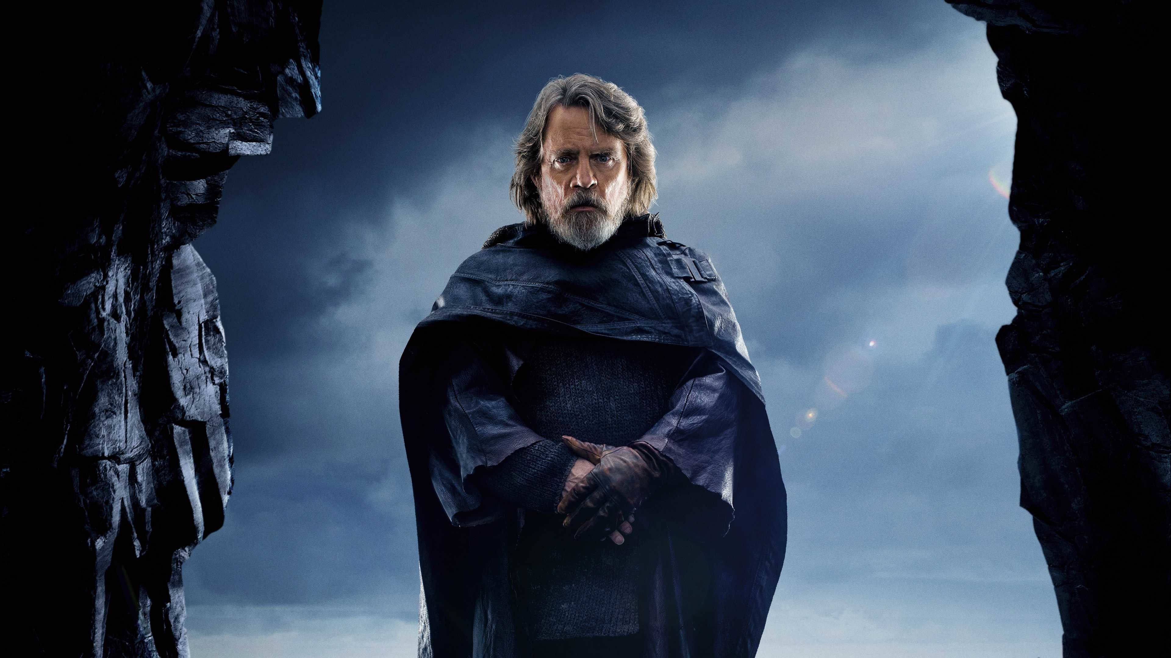 Star Wars Luke Skywalker 4K 桌布 壁紙 — Luke Skywalker 在暴風雨天空下的岩石裂縫中莊嚴地站立，他歷經風霜的臉龐和深色斗篷傳達出沉靜的決心。