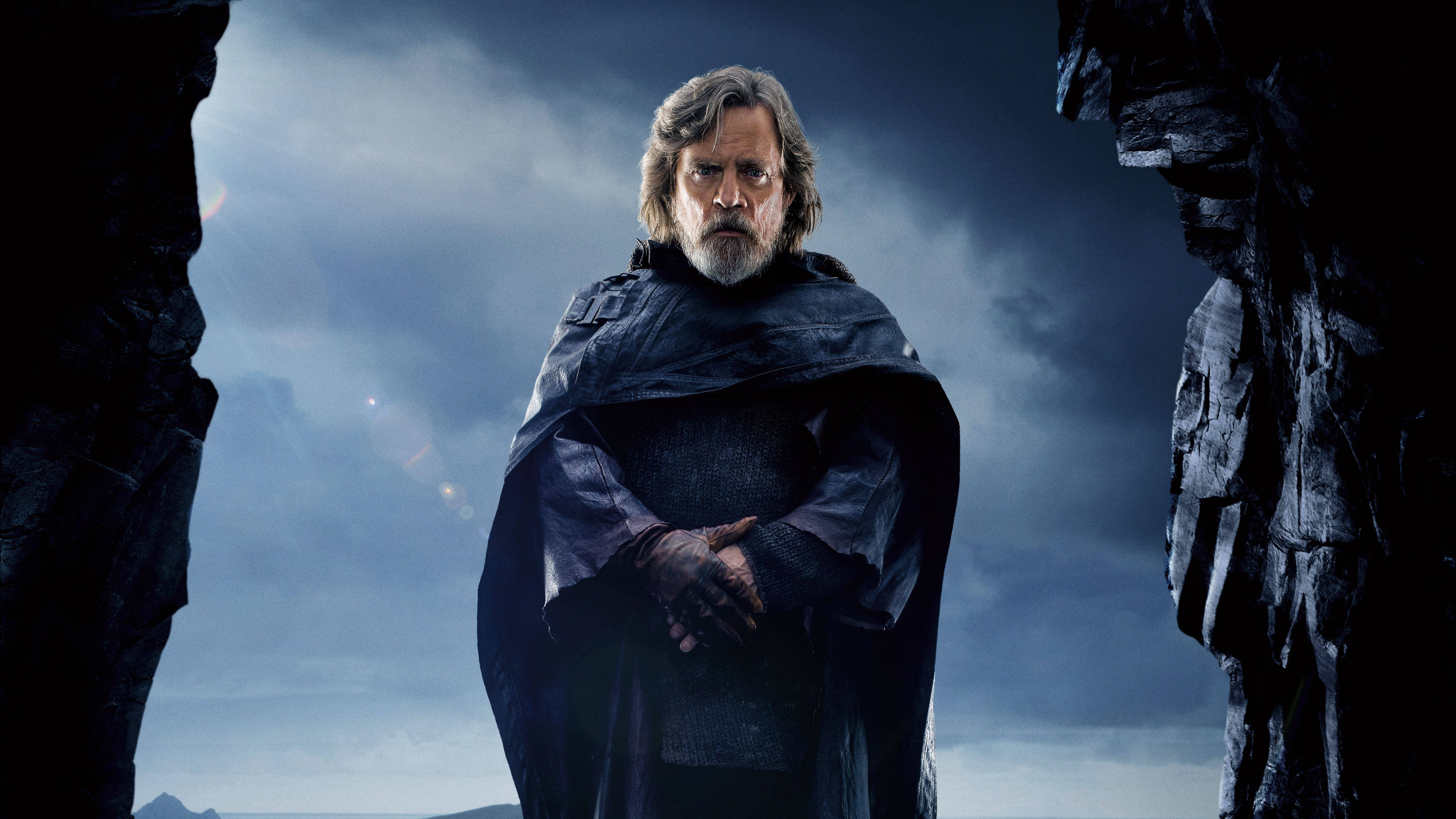 4K 星際大戰 桌布 壁紙 — Luke Skywalker 身穿深色斗篷，莊嚴地站在崎嶇的懸崖之間，背景是風暴籠罩的暮色天空。