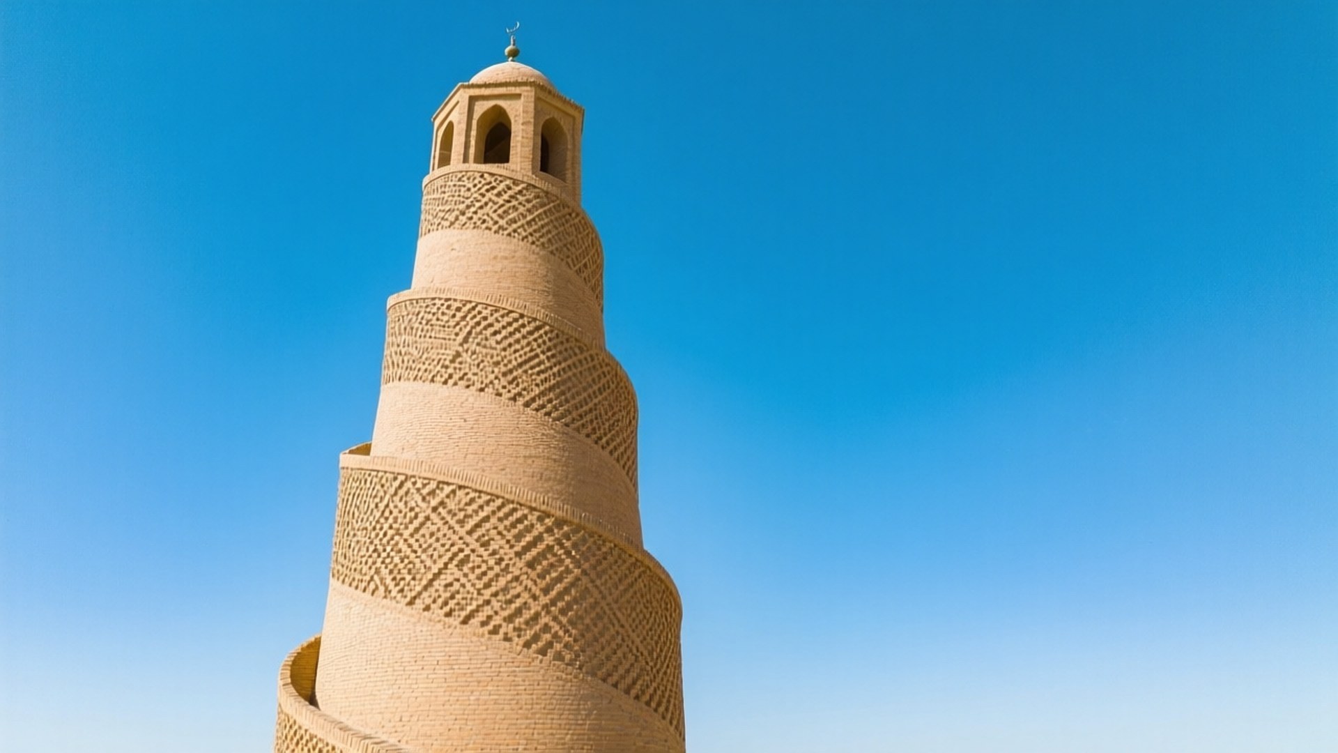 Samarra Spiral Minaret 壁紙 — 一座高大的米色螺旋宣禮塔，帶有複雜的幾何磚砌工藝，在清澈的藍天下聳立。