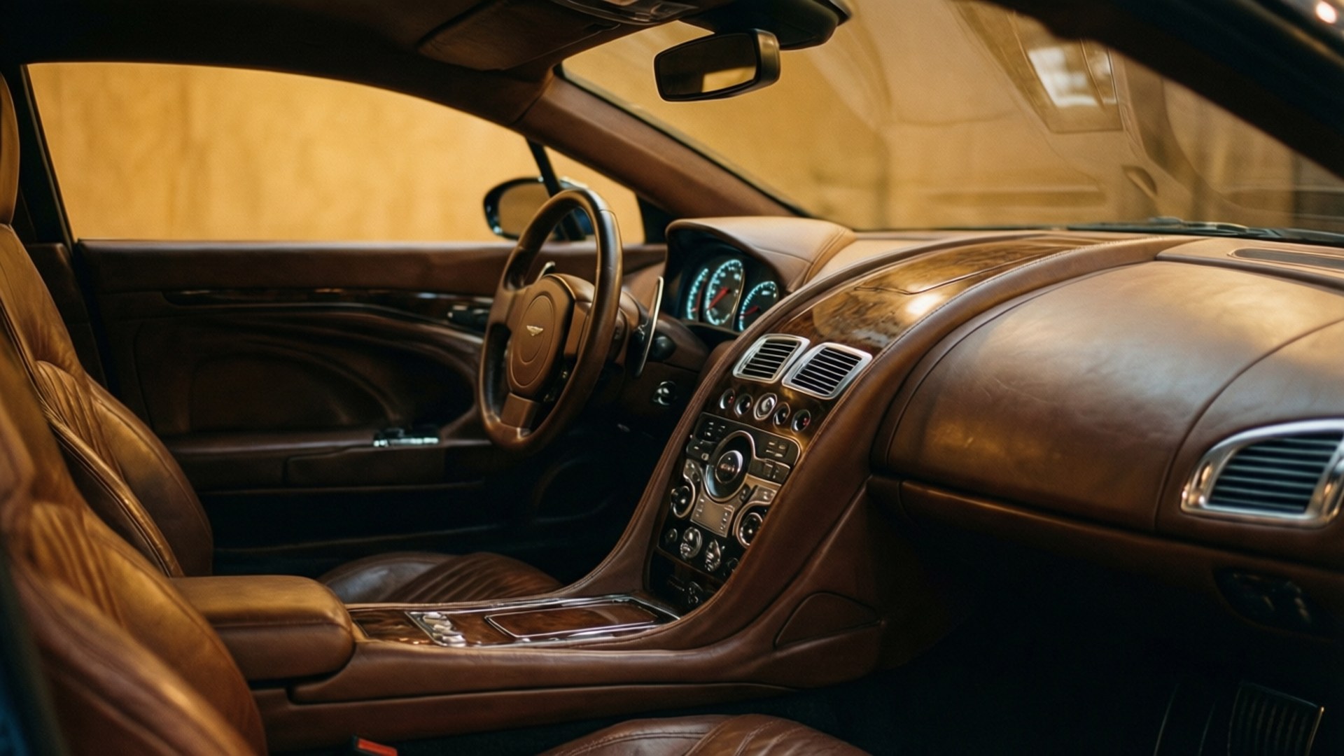 Vanquish Interior Luxury 壁紙 — 豪華車內裝，配有豐富的棕色皮革座椅和儀表板，由發光的藍色儀表組照亮。