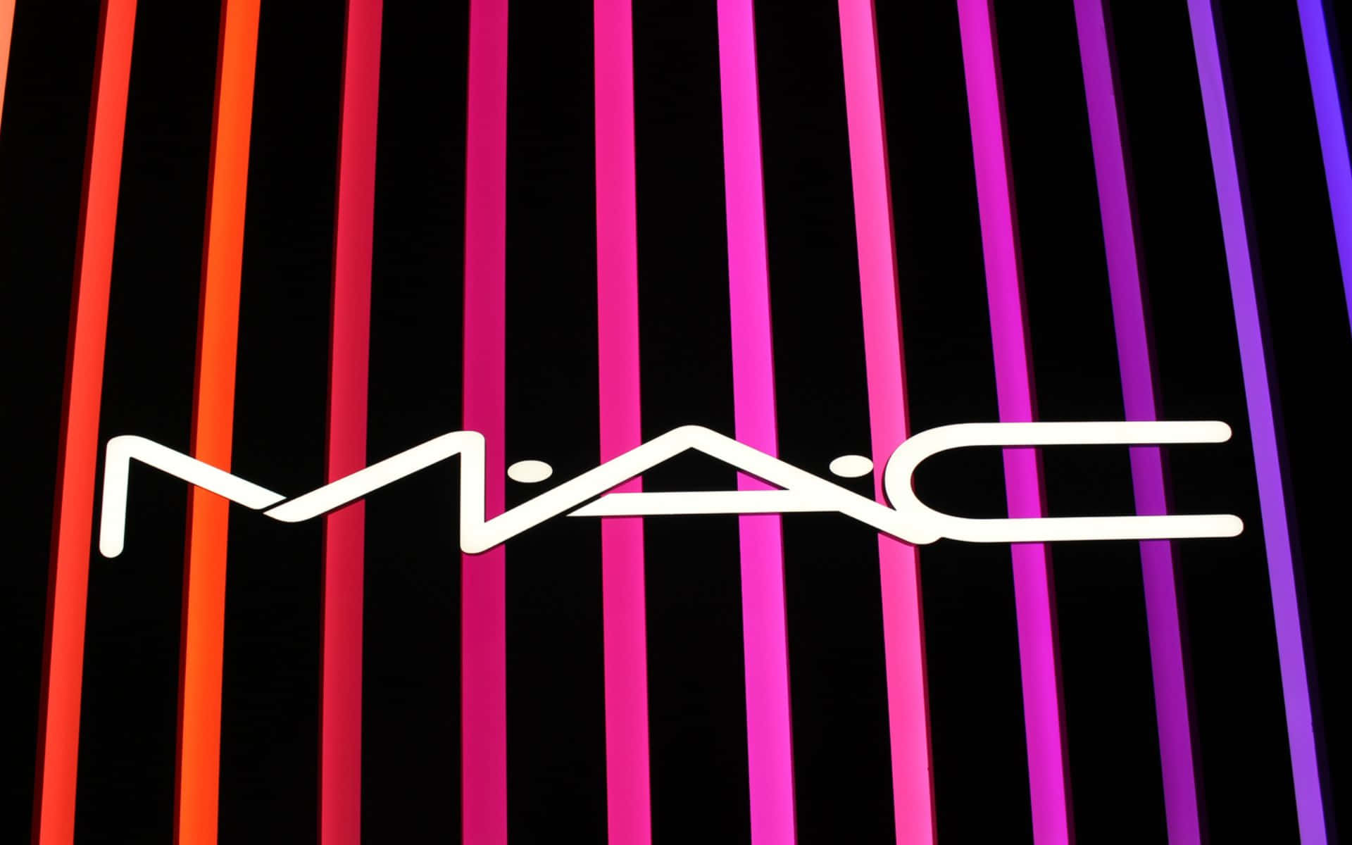 Mac Cosmetics 桌布 壁紙 — MAC 標誌在從橙色到紫色的鮮豔垂直霓虹條紋漸變背景上發出白色光芒。