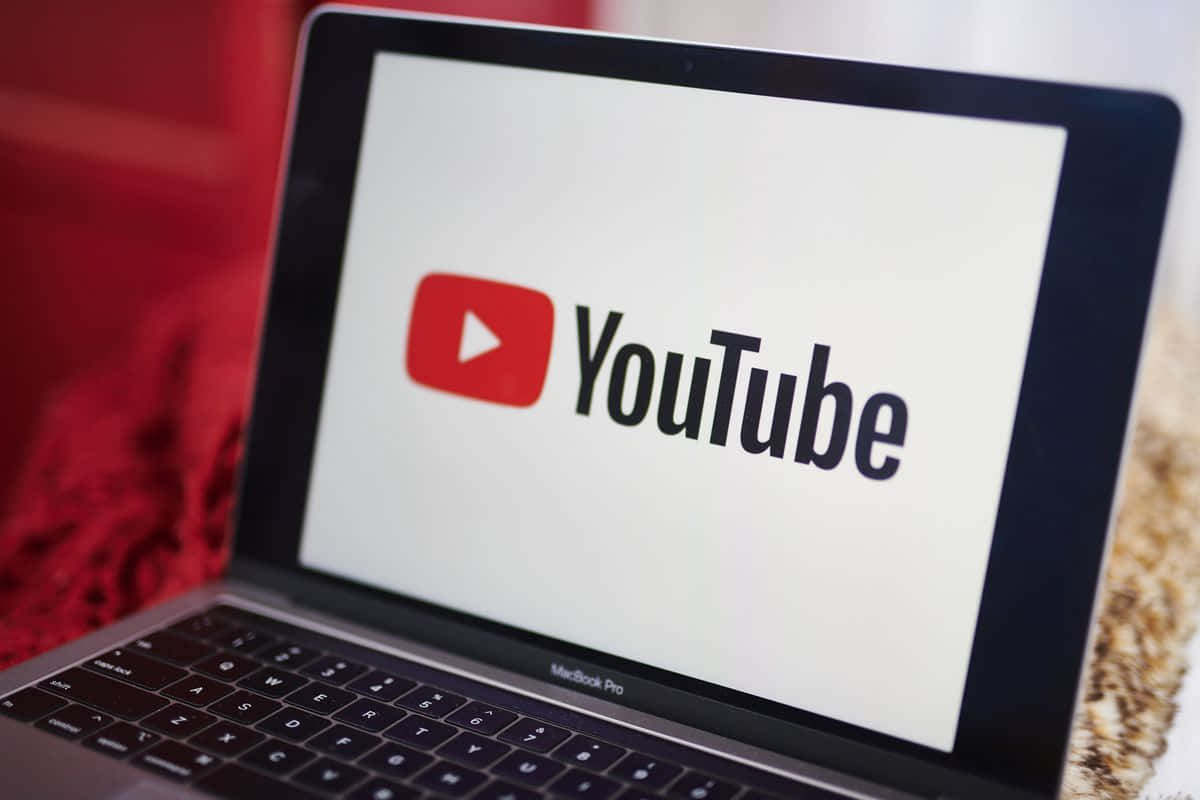 YouTube 桌布 壁紙 — MacBook Pro 的特寫，螢幕上顯示 YouTube 標誌，背景為模糊的紅色和米色。