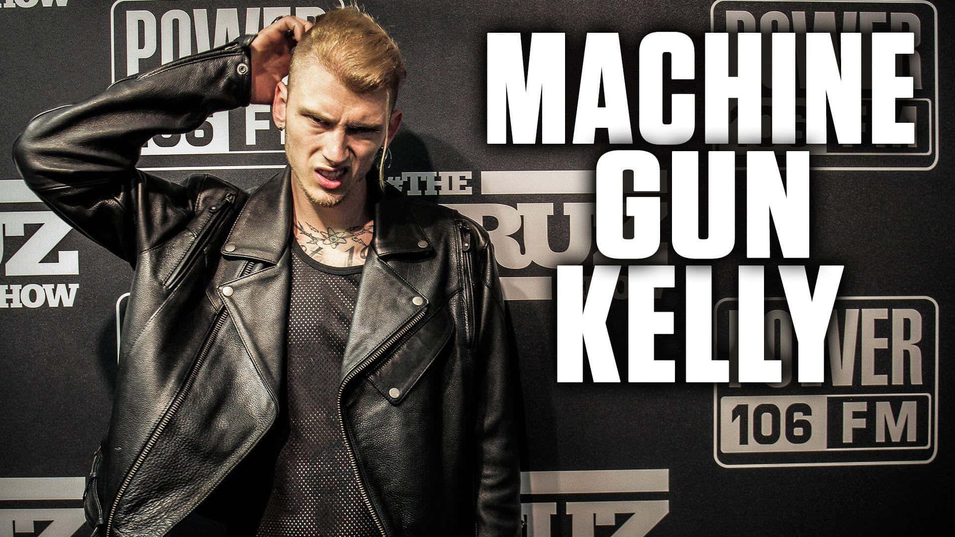 說唱歌手 桌布 壁紙 — Machine Gun Kelly 身穿黑色皮夾克，在印有粗體白色文字的電台品牌背景前擺姿勢。