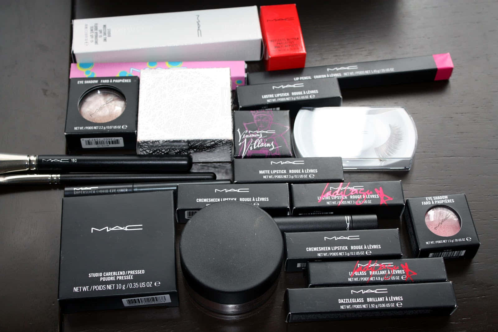 Mac Cosmetics 桌布 壁紙 — MAC化妝品的平鋪擺設，包括唇膏、眼影和刷具，排列在深色木質表面上。