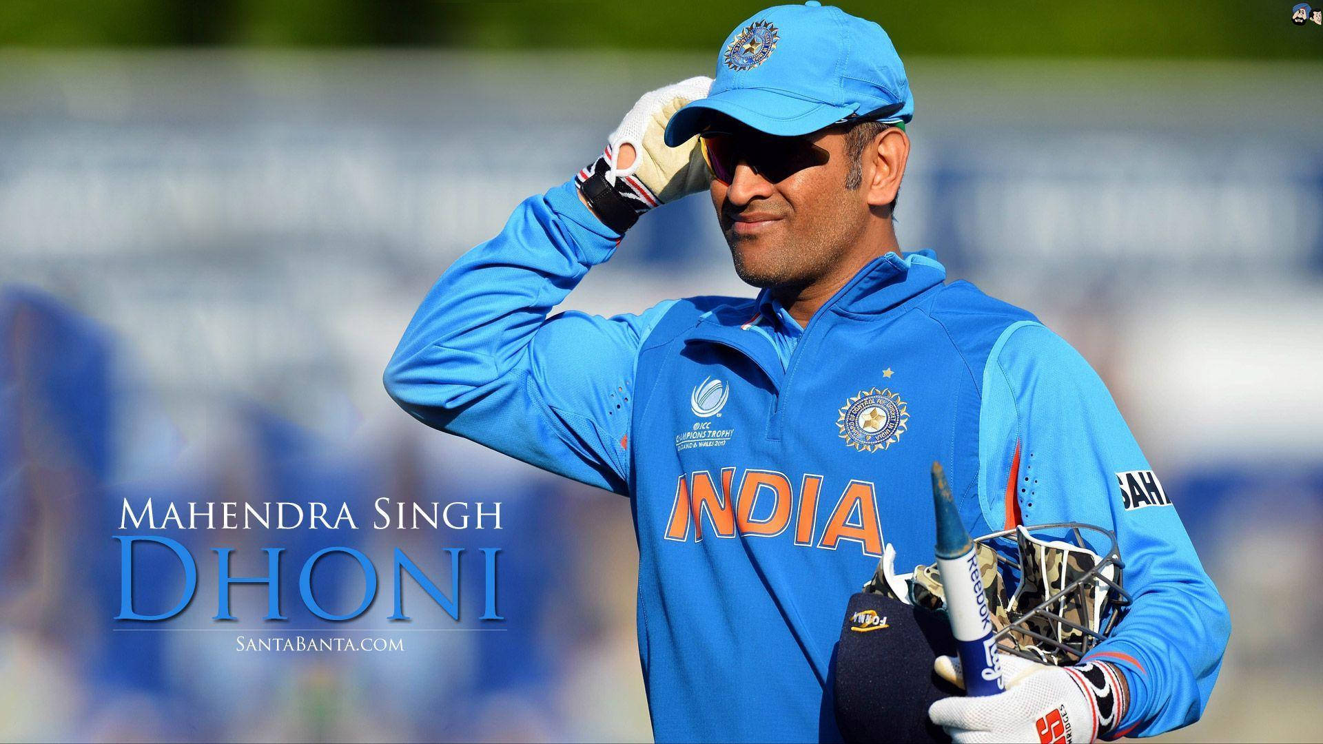 Ms Dhoni 桌布 壁紙 — Mahendra Singh Dhoni 穿著藍色印度板球裝備，在陽光明媚的場地上脫帽致意，手持球棒和頭盔。
