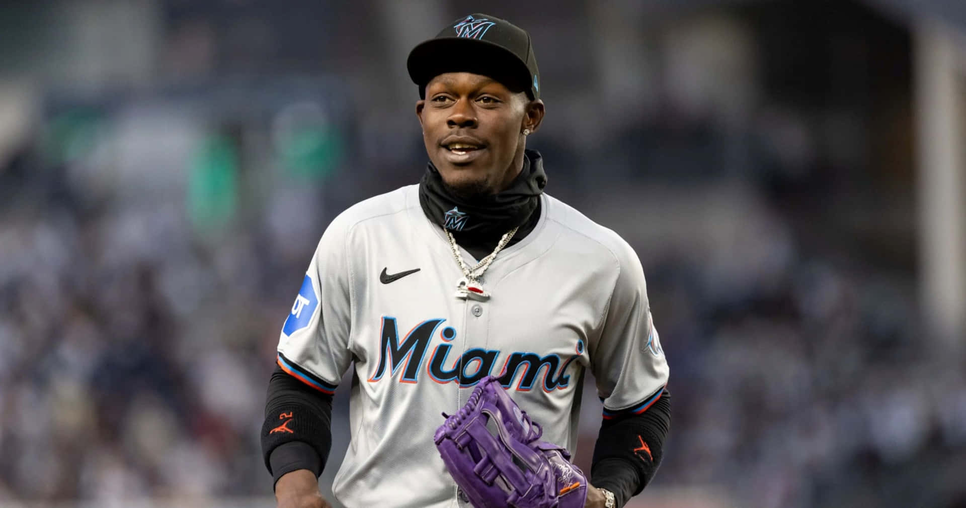  壁紙 — 一名身穿灰色球衣和紫色手套的邁阿密馬林魚棒球選手在球場上行走，背景是模糊的球迷。