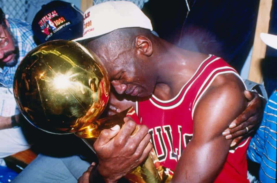 麥可喬丹身穿紅色公牛隊球衣擁抱NBA冠軍獎盃。 — Jordan Logo 壁紙