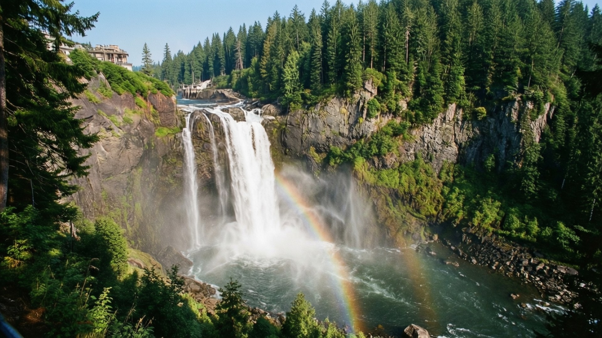 Snoqualmie Falls Splendor 壁紙 — 一道壯麗的瀑布從岩石峽谷中傾瀉而下，周圍是茂密的常綠森林，一道鮮豔的彩虹在下方霧氣瀰漫的水潭上空拱起。