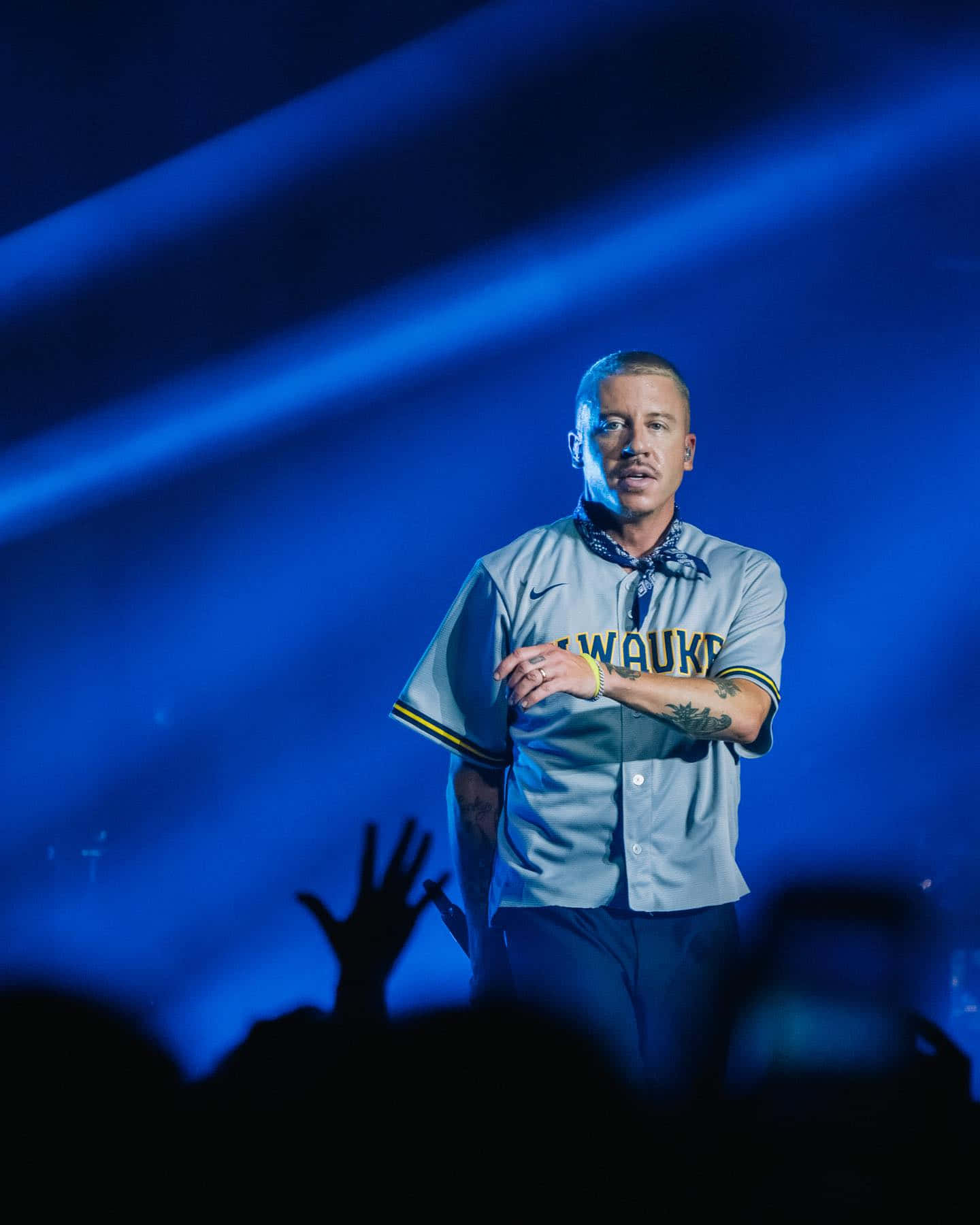  壁紙 — 一位身穿密爾瓦基棒球球衣的男性表演者站在舞台中央，在戲劇性的藍色聚光燈下，下方有觀眾舉起雙手。