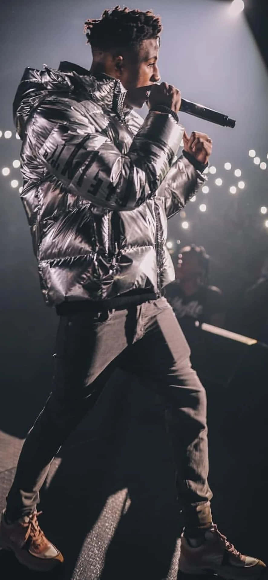 男性歌手穿著銀色羽絨外套在明亮的燈光下進行舞台表演。 — NBA Youngboy 壁紙
