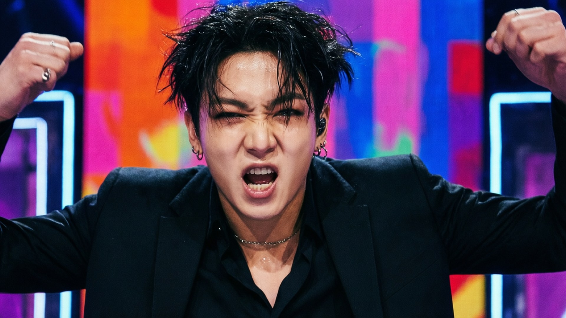 G-Dragon 桌布 壁紙 — 一位深色頭髮、身穿黑色西裝的男表演者，在充滿活力的霓虹燈舞台背景下，激情地高舉拳頭吶喊。