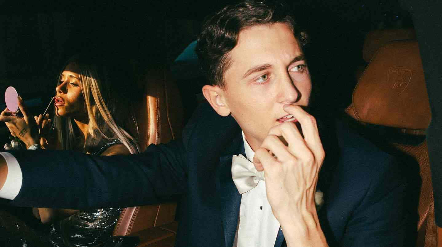  壁紙 — 一名身穿燕尾服的男士正在塗口紅，而一名身穿亮片裙的女士在夜晚的豪華車內化妝。