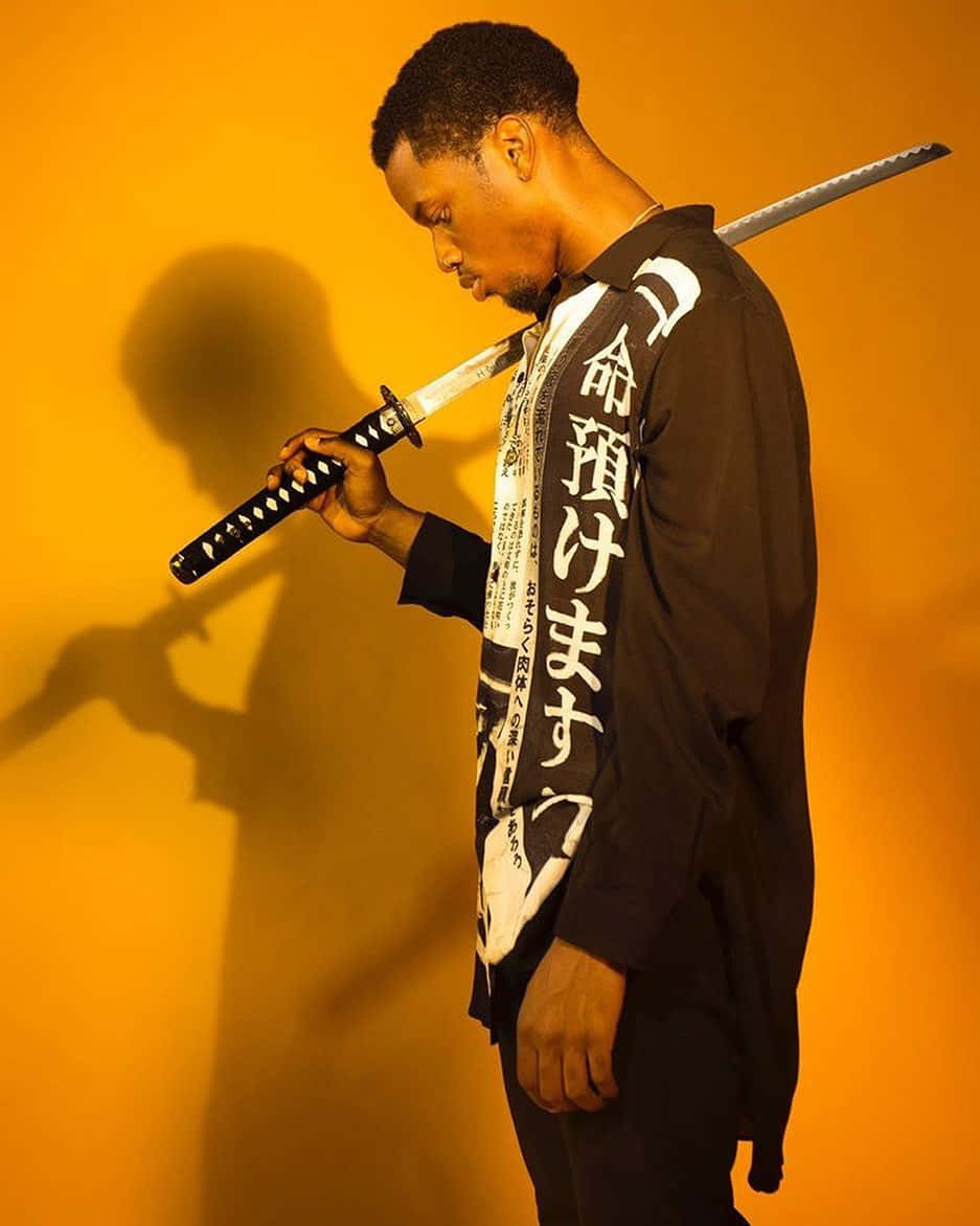  壁紙 — 一名身穿黑色和服、帶有日文字的男子，手持武士刀，靠著溫暖的橙色工作室牆壁，投射出戲劇性的陰影。