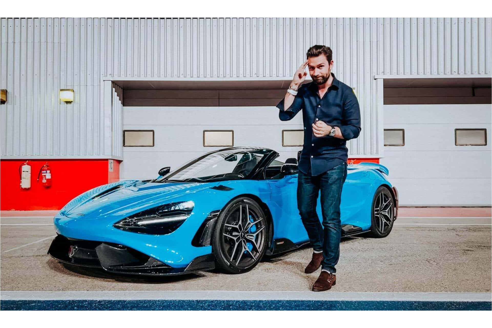 Mclaren 765lt 桌布 壁紙 — 一名身穿深色襯衫的男子自信地站在現代工業車庫中一輛充滿活力的藍色跑車旁。