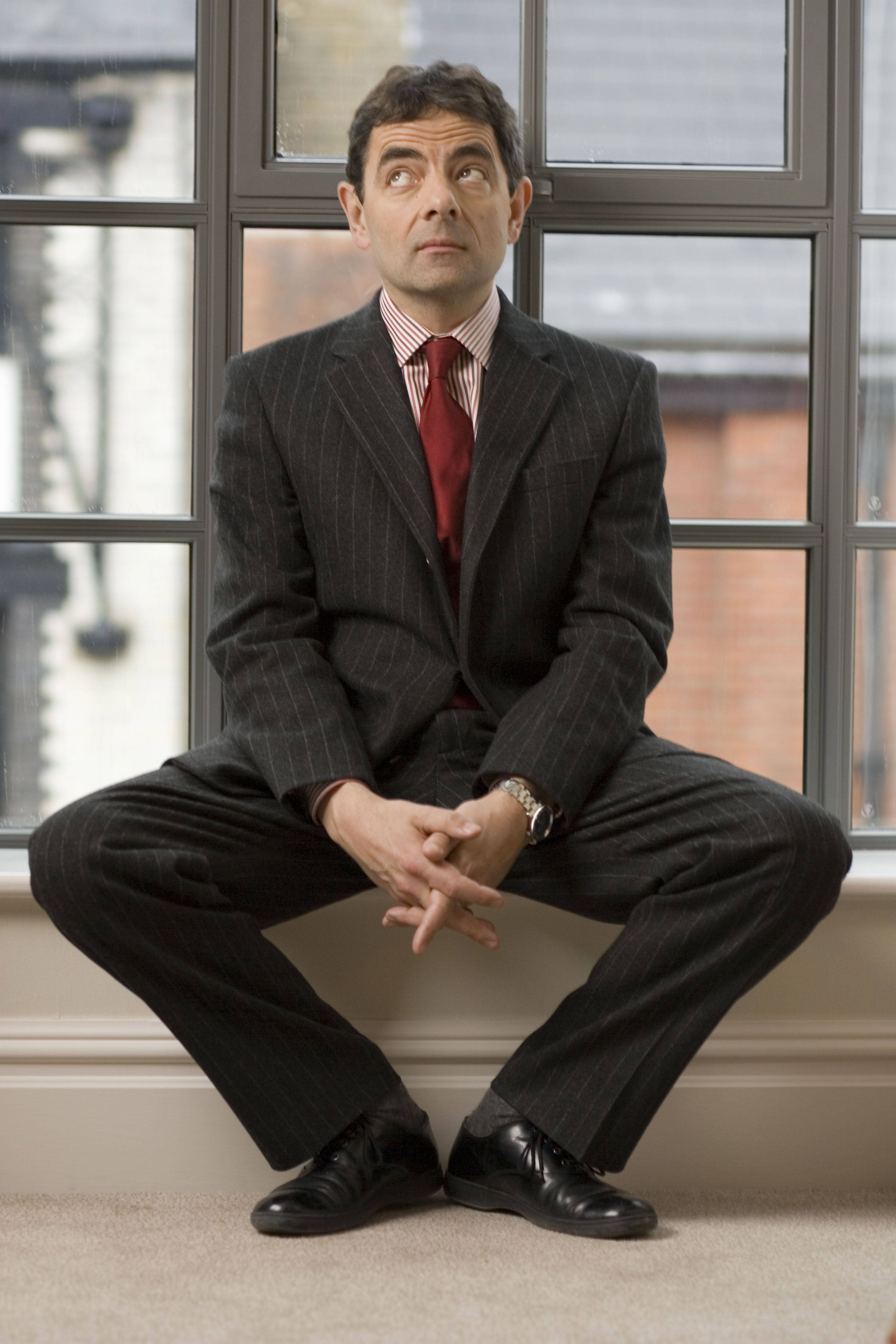 穿著細條紋西裝的男人坐在窗台上向上看，表情困惑。 — 4K 壁紙
