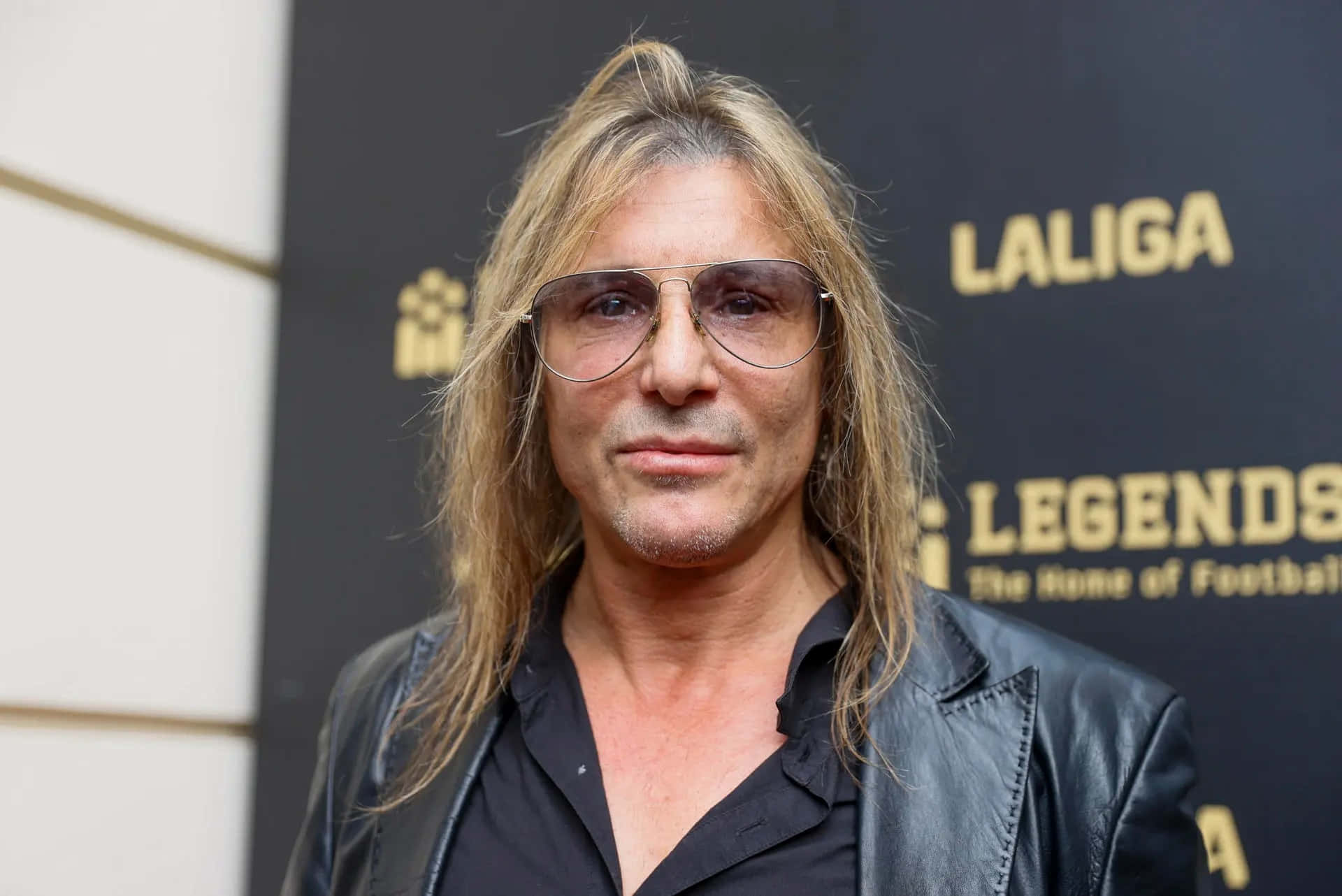  壁紙 — 一位長金髮、戴飛行員太陽眼鏡的男子，身穿黑色皮夾克在Laliga Legends活動中擺姿勢。