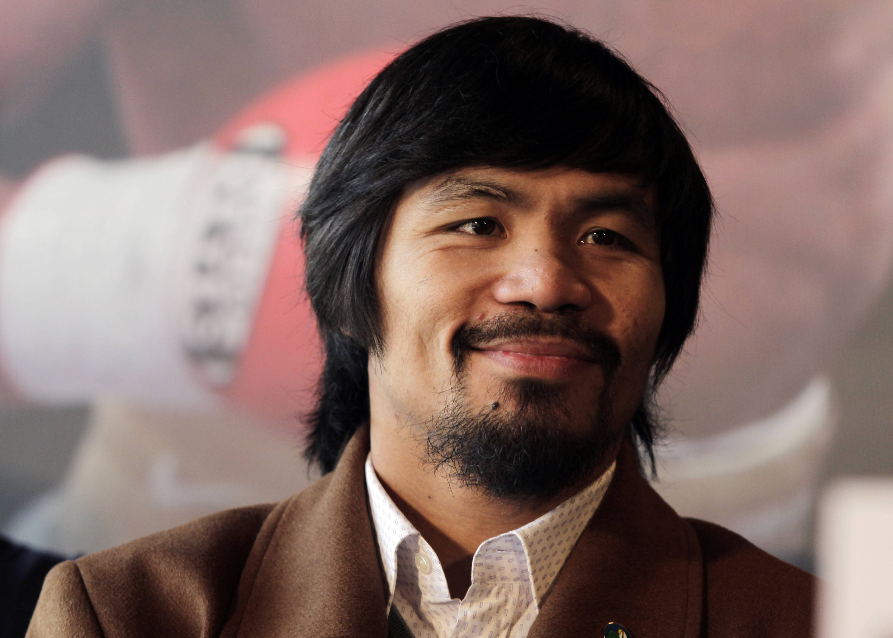 微笑 桌布 壁紙 — Manny Pacquiao 的特寫肖像，他穿著棕色外套，在模糊的拳擊主題背景前溫暖地微笑。