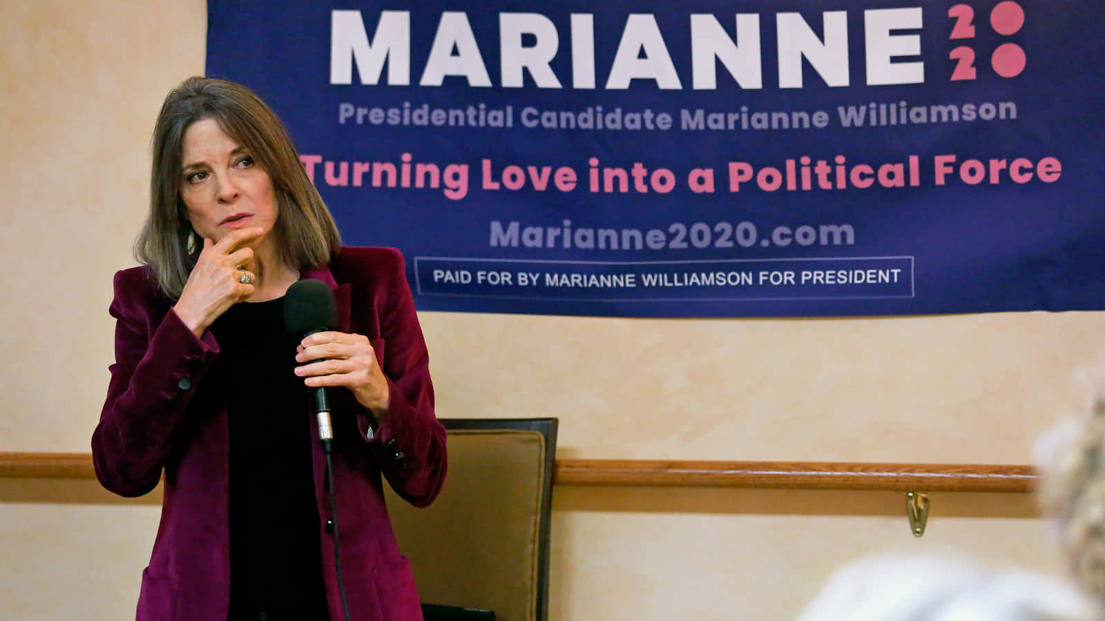 政治 桌布 壁紙 — Marianne Williamson 身穿栗色西裝外套，在2020年總統競選活動中對著麥克風講話。