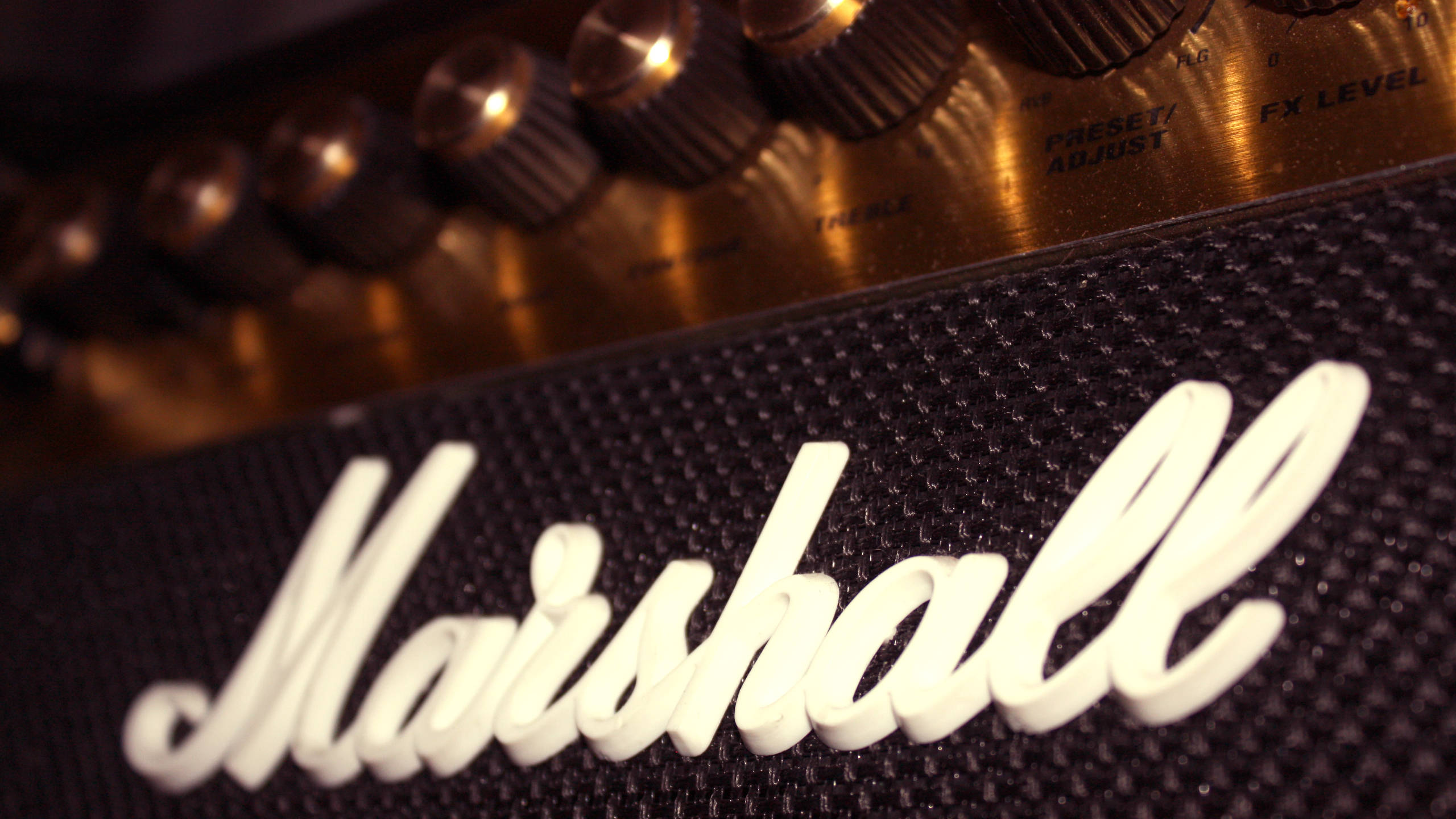 Marshall 桌布 壁紙 — Marshall吉他擴大機的特寫，具有發光旋鈕和紋理格柵布，在溫暖燈光下。