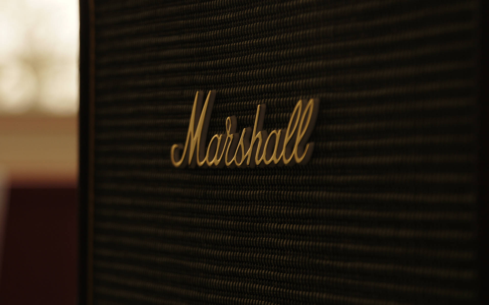 Marshall 桌布 壁紙 — Marshall擴音器特寫，金色標誌位於紋理黑色格柵上，背景溫暖模糊。