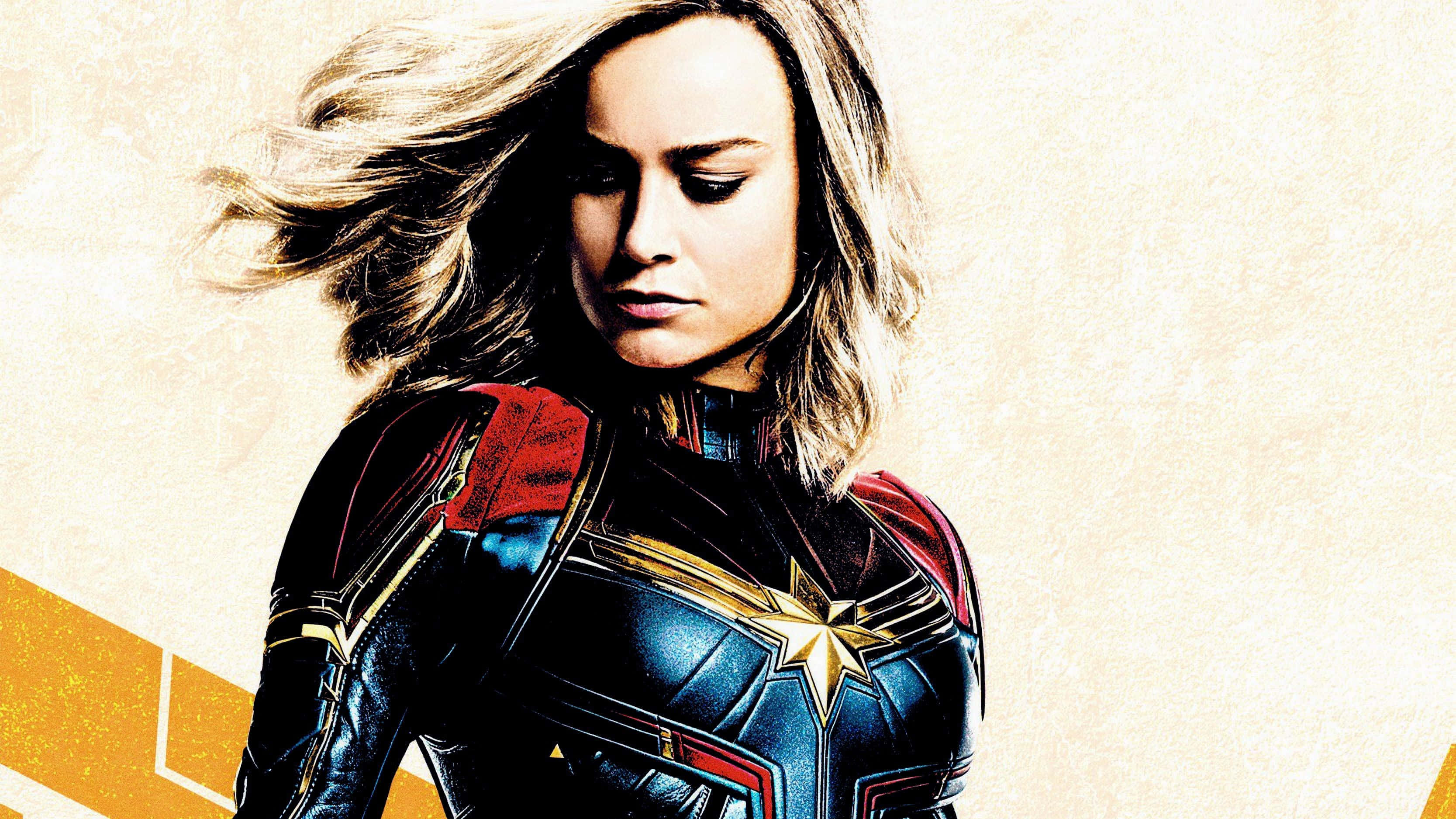 Captain Marvel 桌布 壁紙 — Marvel 隊長身穿藍、紅、金色戰衣，頭髮隨風飄揚，背景為帶紋理的米色。