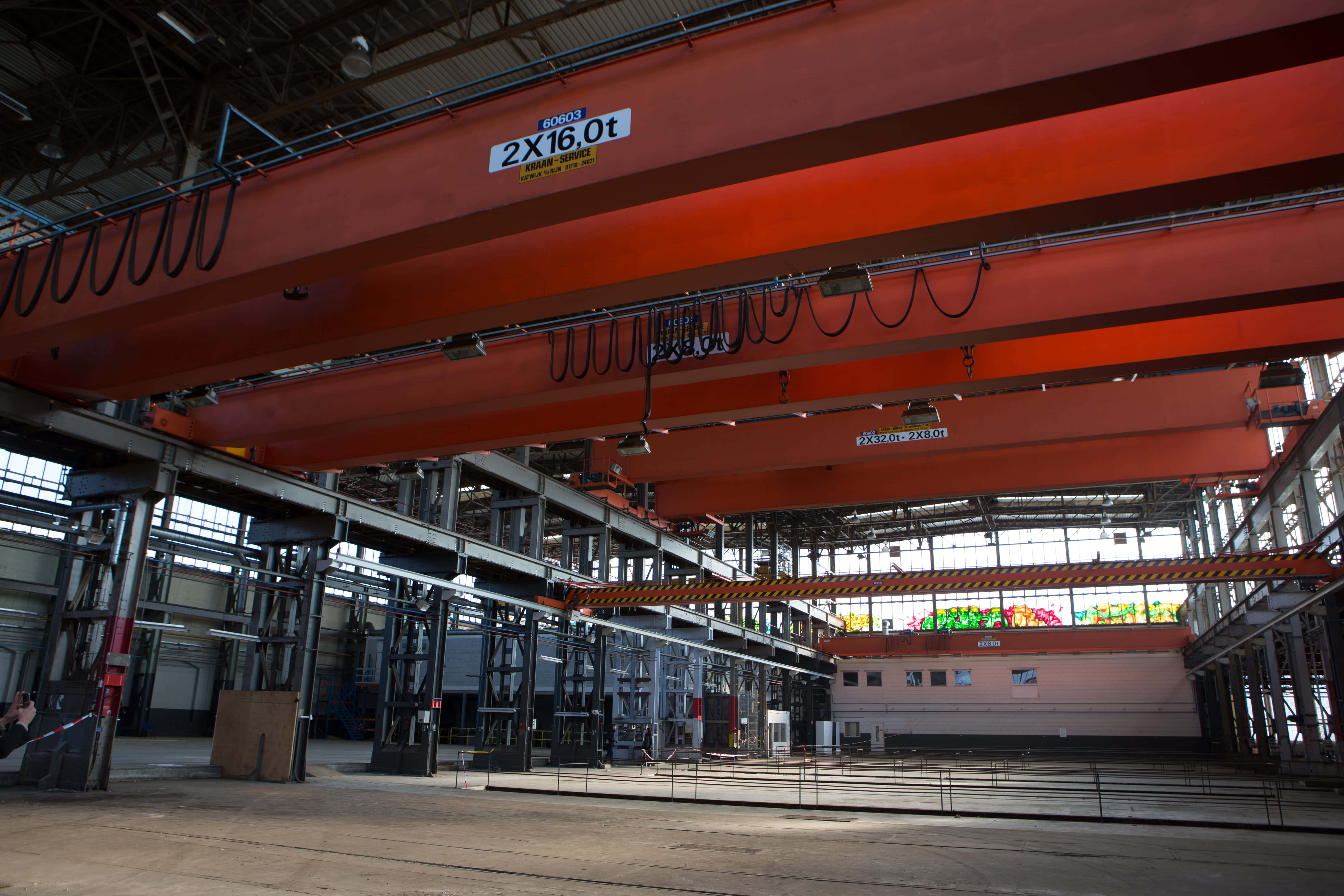 Tilburg 桌布 壁紙 — 巨大的橙色工業起重機在寬敞的鋼鐵廠中高聳，廠房擁有高天花板和自然光。