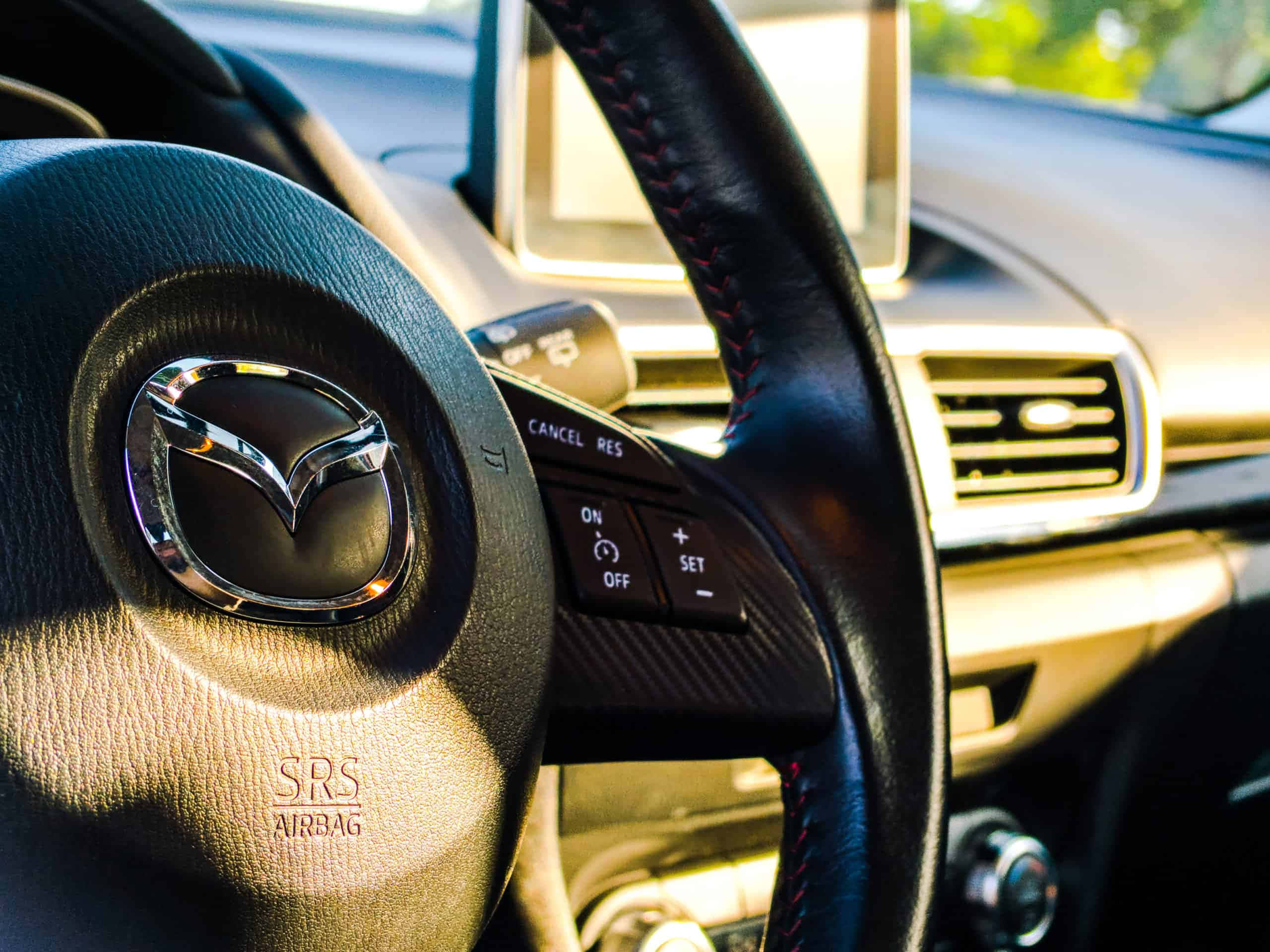 Car Technology 桌布 壁紙 — Mazda 方向盤特寫，紅色縫線及鍍鉻徽章沐浴在溫暖陽光下。