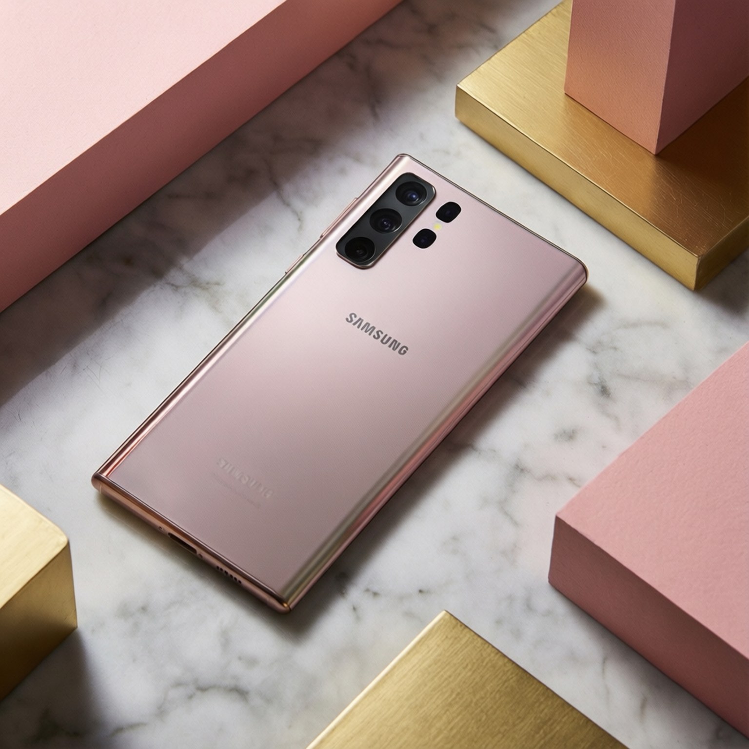 Elegant Note 10 壁紙 — 一支玫瑰金三星智慧型手機優雅地放置在白色大理石表面上，周圍環繞著幾何形狀的粉紅色和金色方塊。