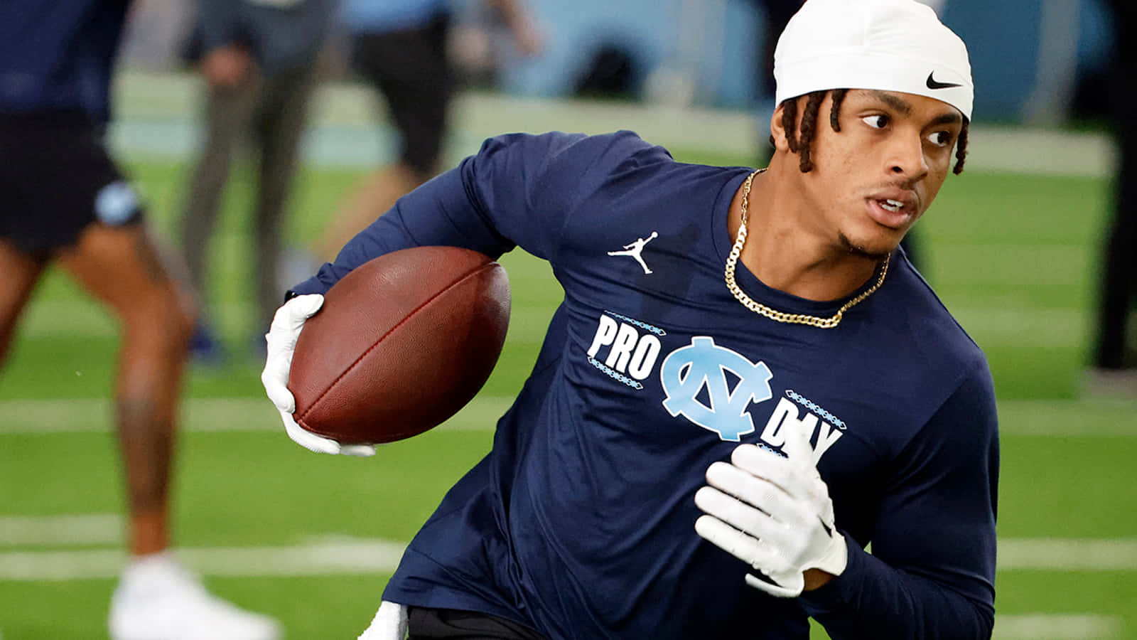  壁紙 — 一名身穿海軍藍「Pro Day」球衣的美式足球員，在綠色球場上拿著棕色足球衝刺。