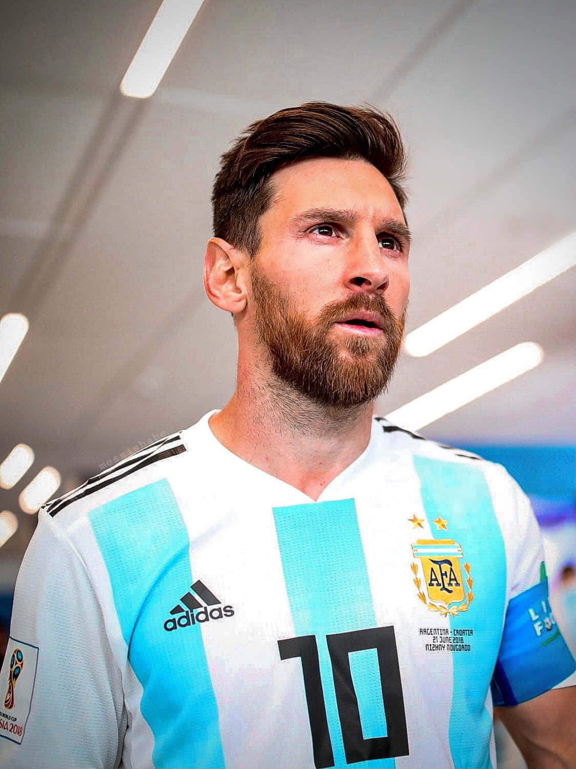 Messi 2022 桌布 壁紙 — 梅西身穿阿根廷藍白條紋球衣，在明亮的燈光下專注地向上凝視。