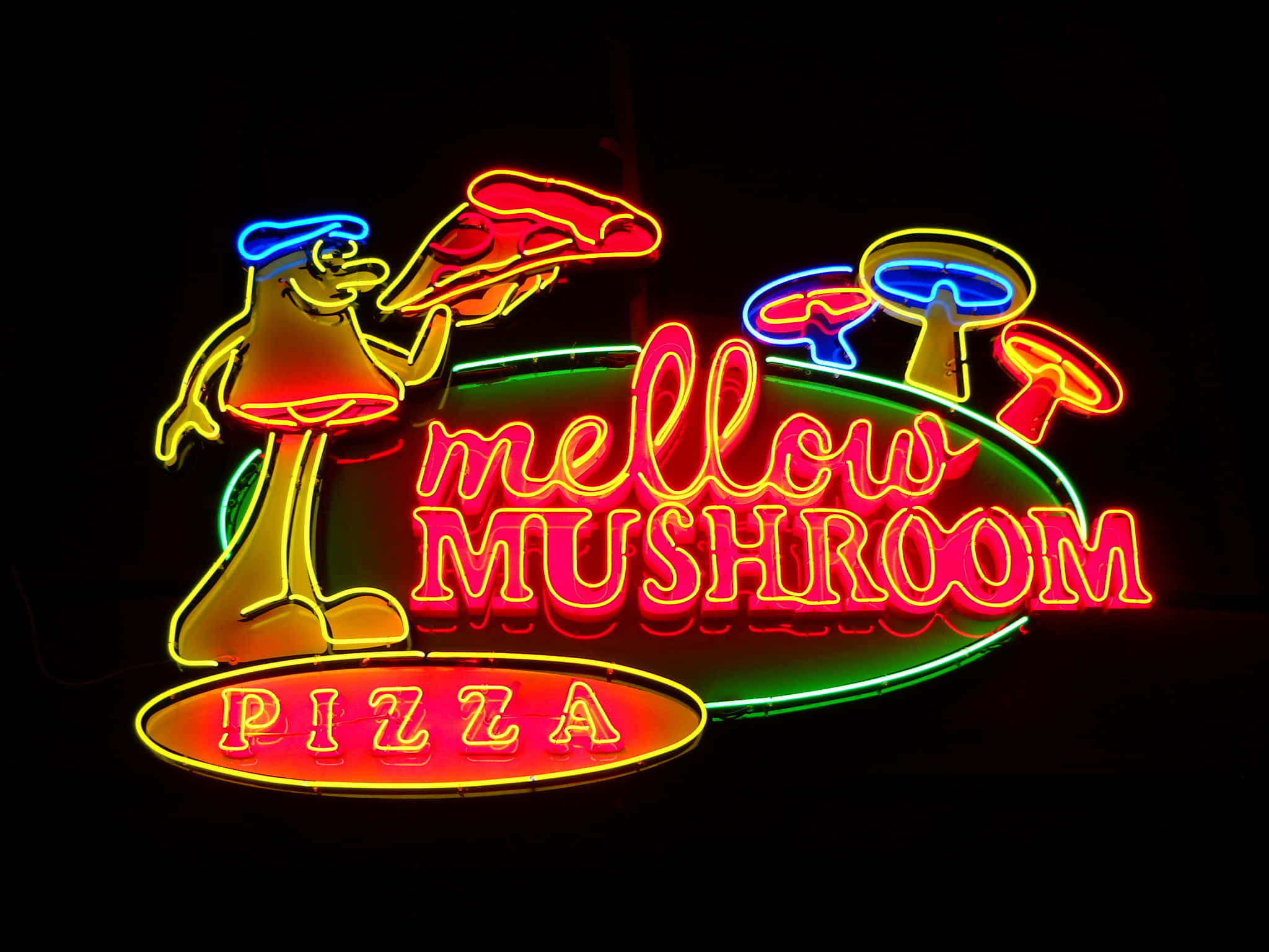 neon sign 桌布 壁紙 — Mellow Mushroom Pizza 的鮮豔霓虹招牌，以深色背景襯托一個拿著披薩片的卡通蘑菇角色。