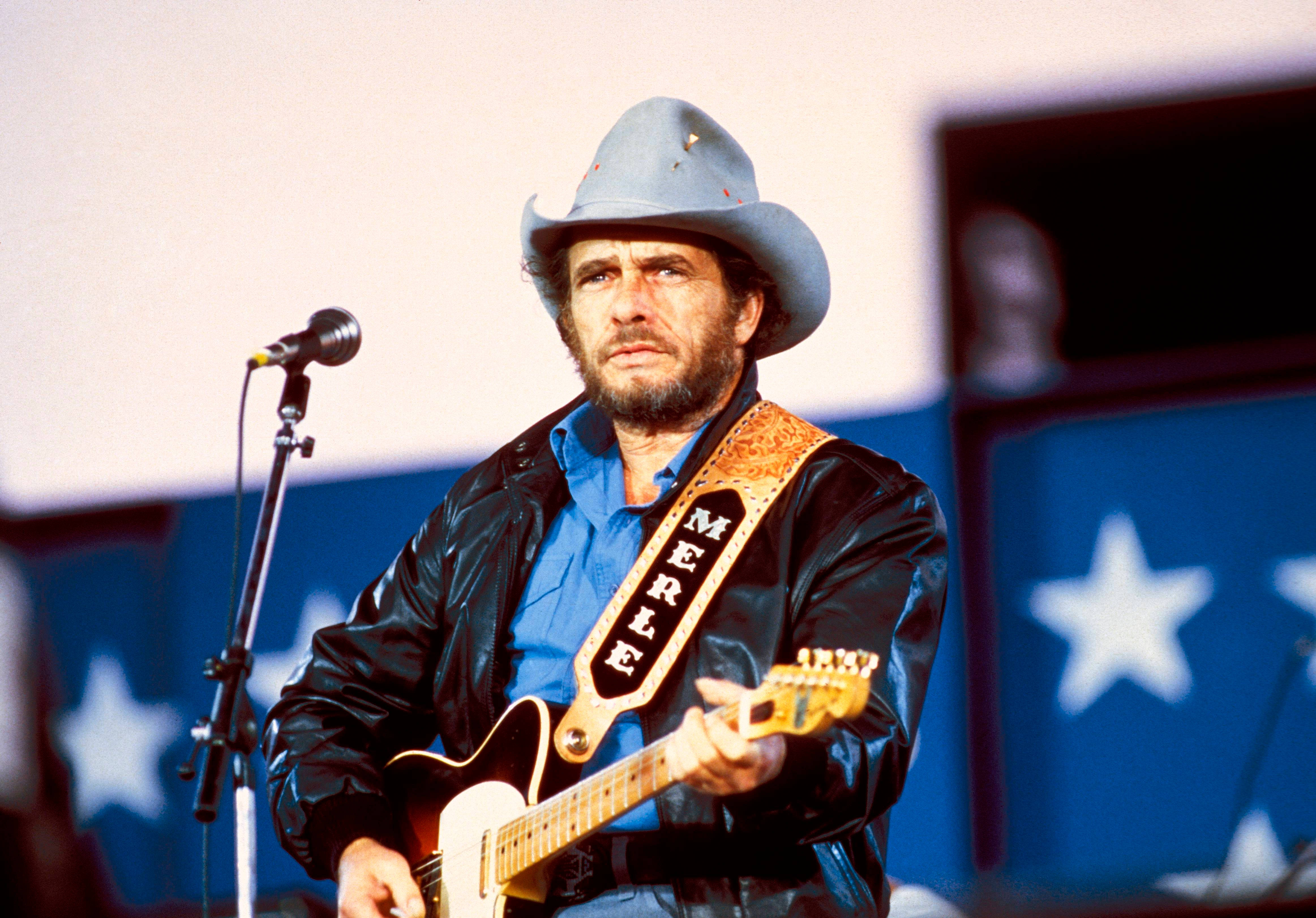 音樂 桌布 壁紙 — Merle Haggard 在舞台上表演，戴著牛仔帽和皮夾克，手持電吉他。
