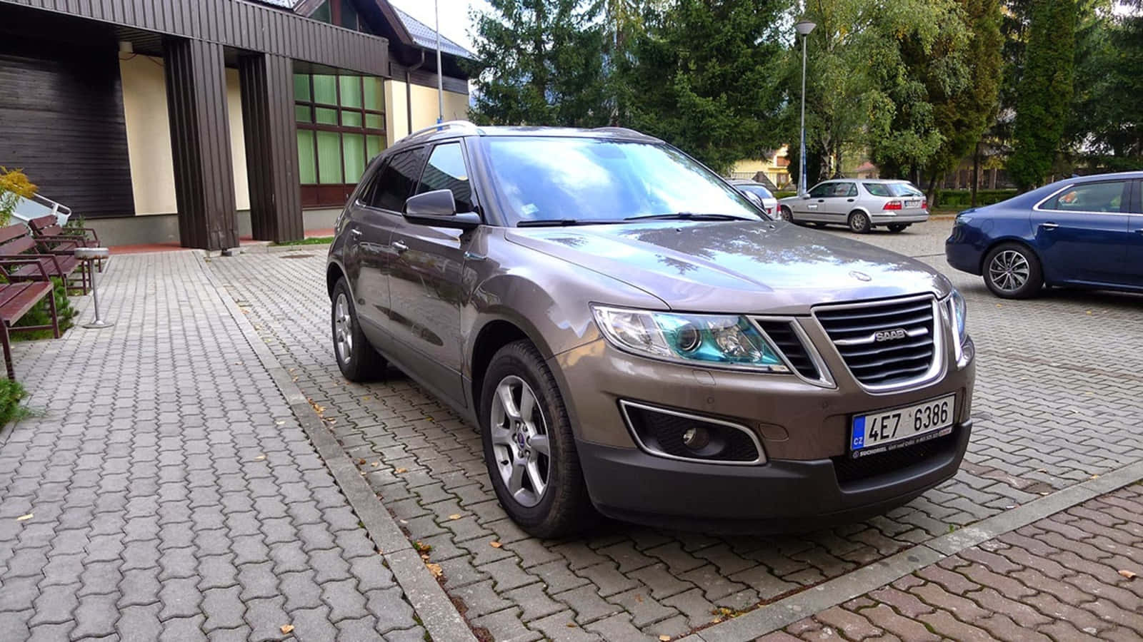 Saab 9-4x 桌布 壁紙 — 一輛金屬棕色薩博SUV停放在灰色磚砌車道上，旁邊是一座帶有綠色窗戶的現代建築。