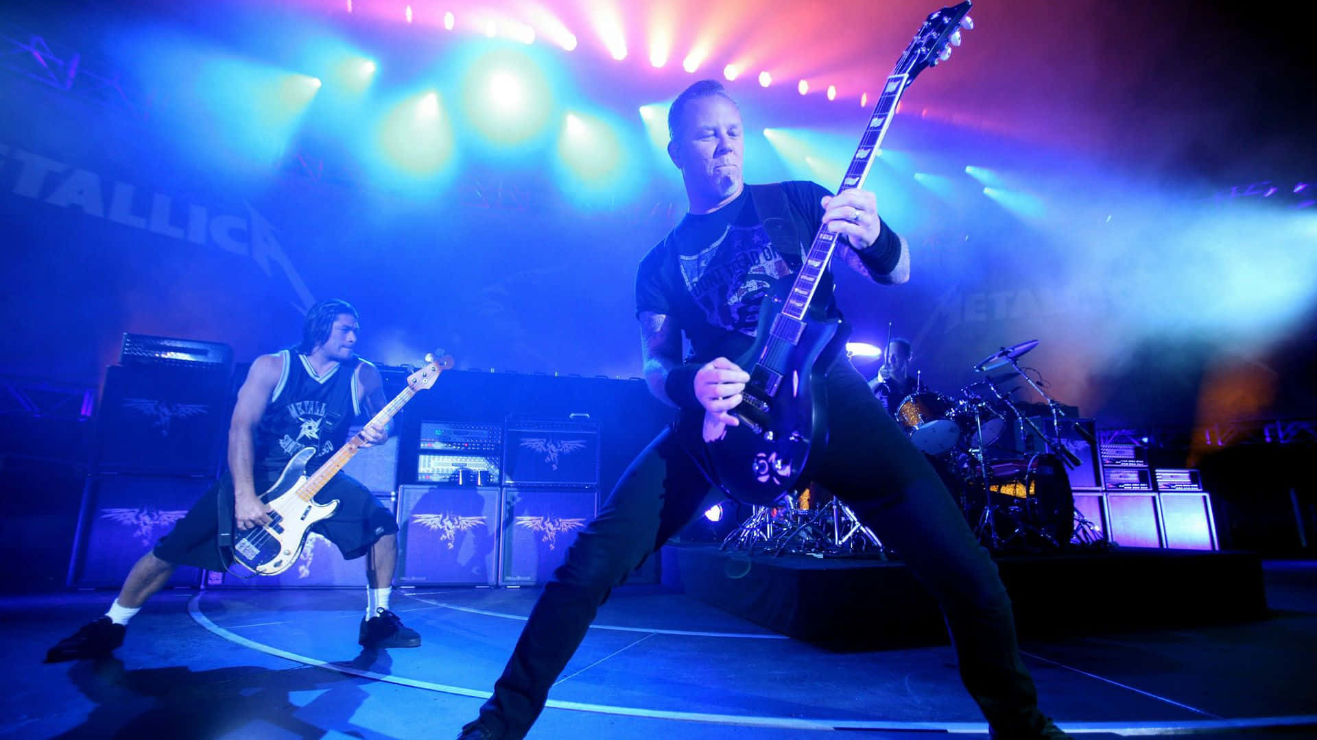 金屬製品樂團 桌布 壁紙 — Metallica 樂團成員在充滿藍色和紫色燈光及煙霧效果的舞台上激烈演出。