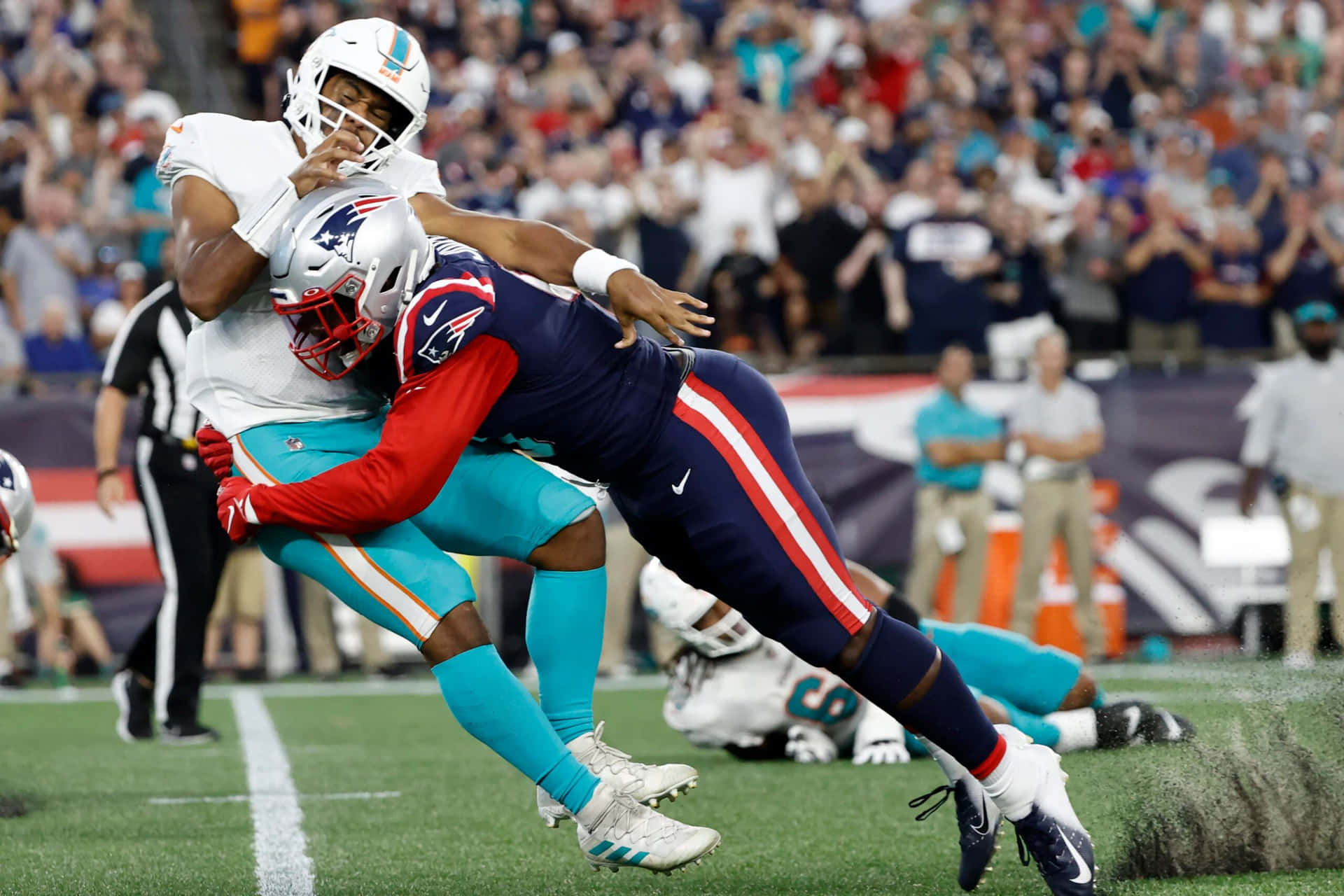  壁紙 — 邁阿密海豚隊的四分衛在緊張刺激的NFL比賽中被新英格蘭愛國者隊的防守球員在半空中擒抱。